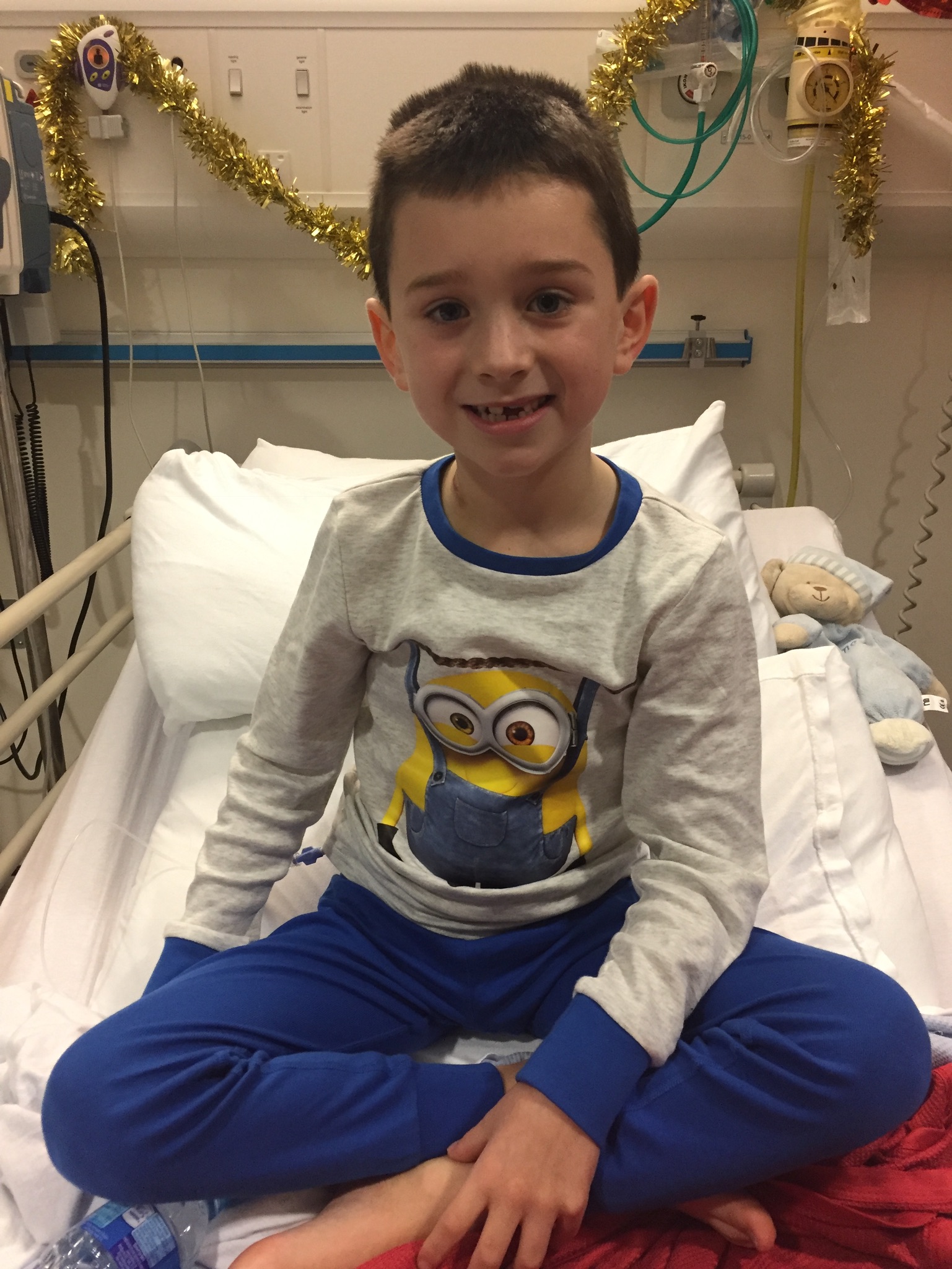 Daniel sat up in a hospital bed, smiling at the camera, wearing Minion pyjamas