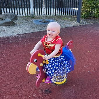 Indy in her Super Woman costume on a rocking horse type play ground equipment
