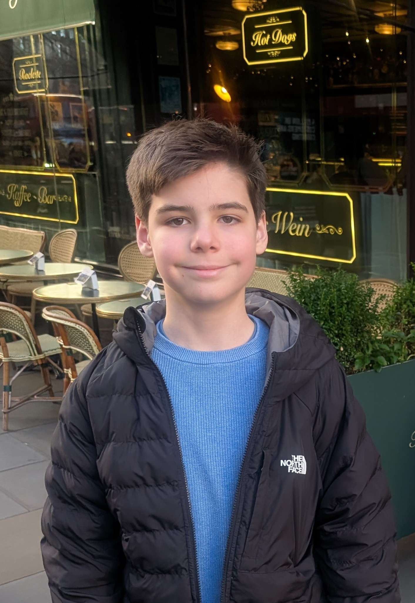 Jack wearing a blue t shirt and dark coat outside a cafe.