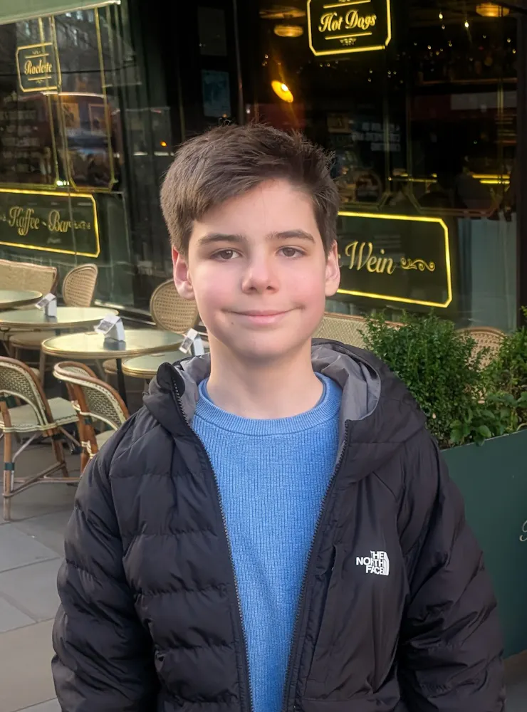 Jack wearing a blue t shirt and dark coat outside a cafe.