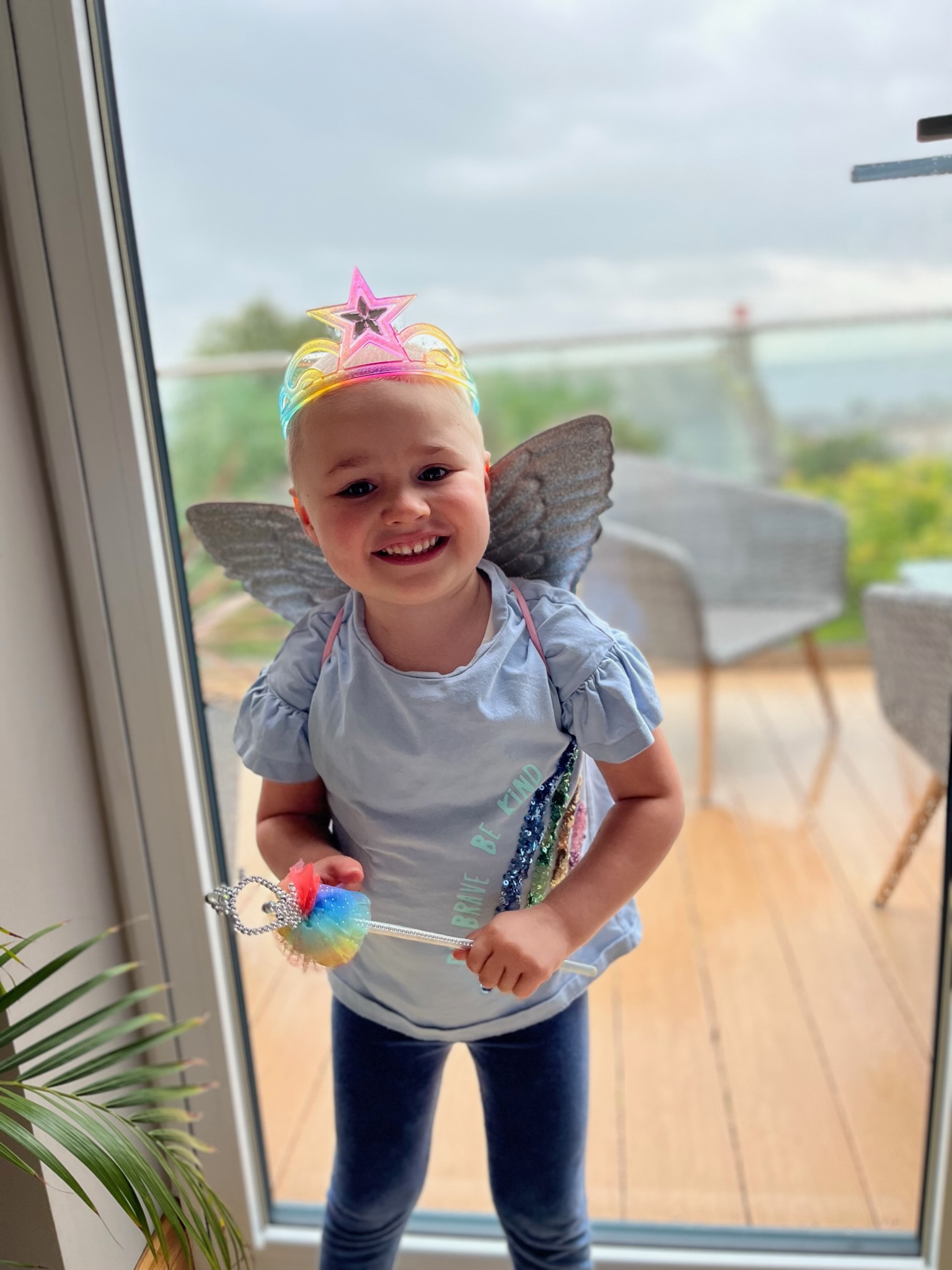 A photo of Emmy standing in front of a glass door. Emmy is wearing wings and a crown. 