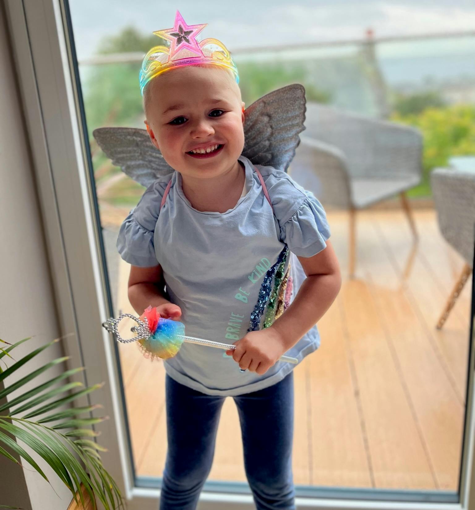 A photo of Emmy standing in front of a glass door. Emmy is wearing wings and a crown.