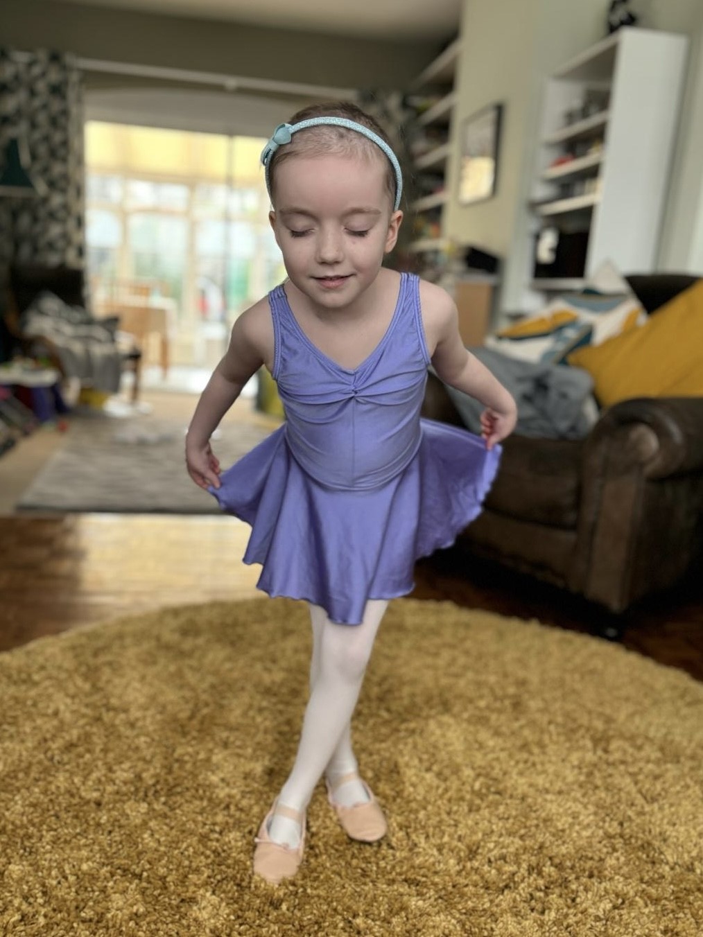 Ava dressed as a ballerina (pink ballet shoes and blue ballerina dress) is bowing with her eyes closed. 