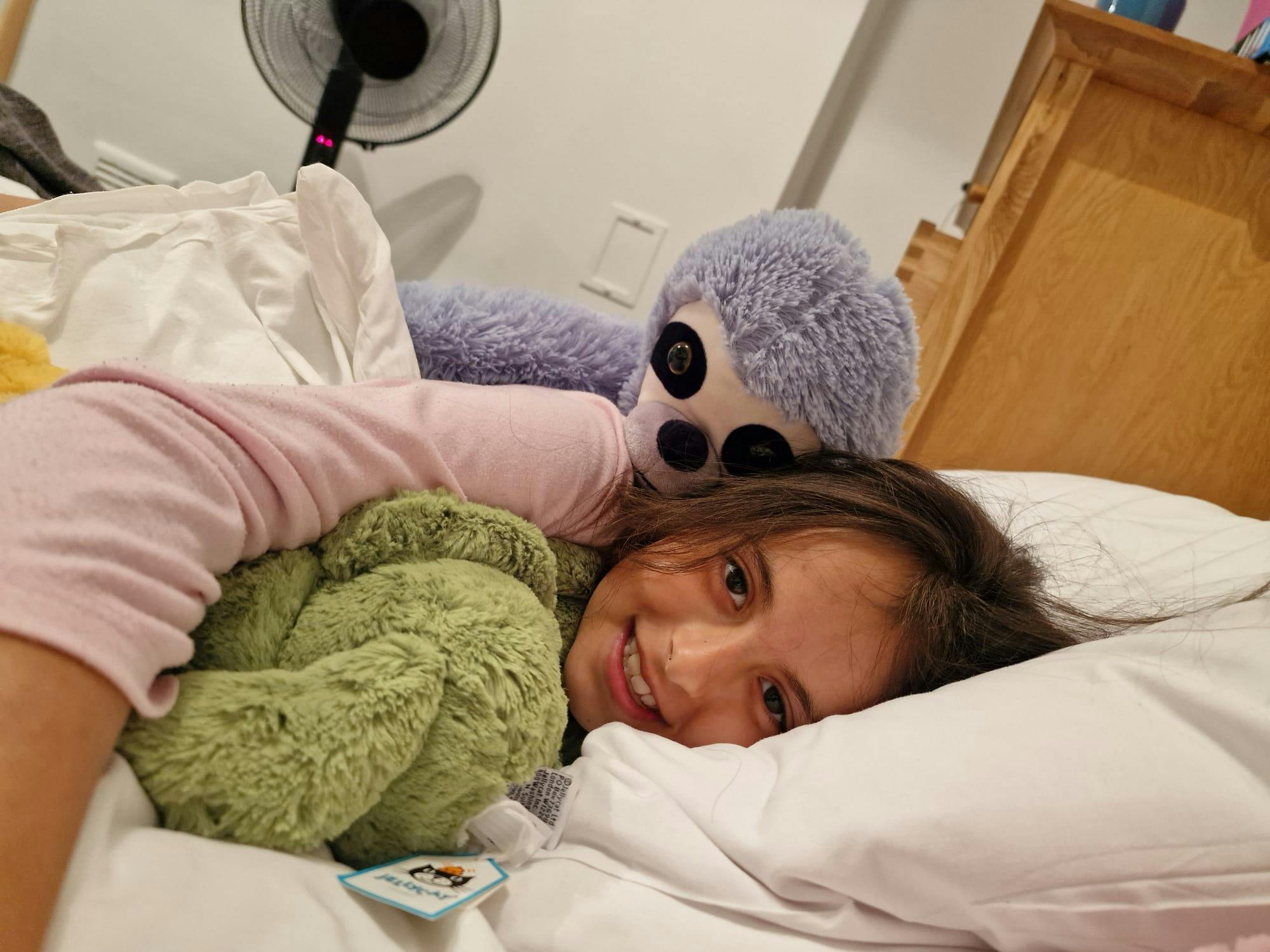 Xanthia lying in bed, smiling, cuddling her soft toys