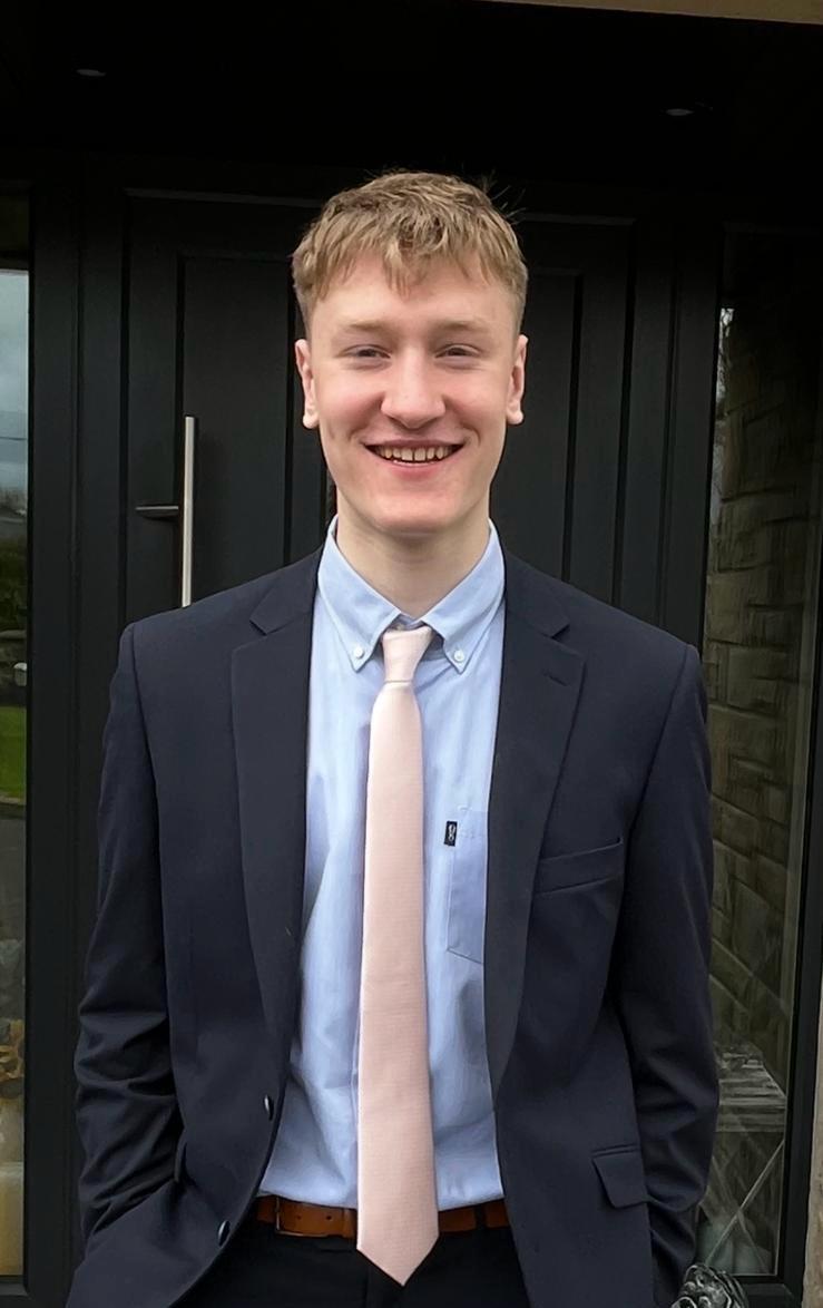 Aaron in a suit smiling with hands in his pocket