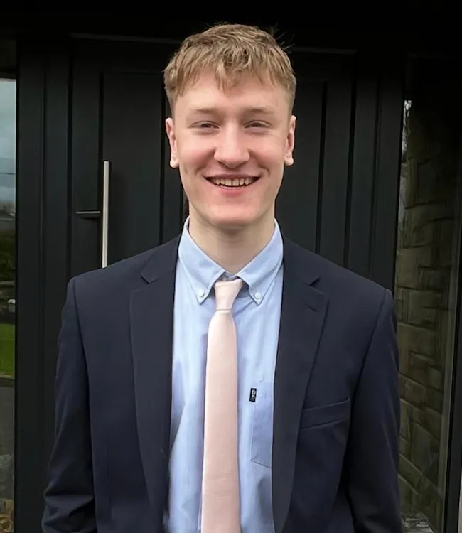 Aaron in a suit smiling with hands in his pocket