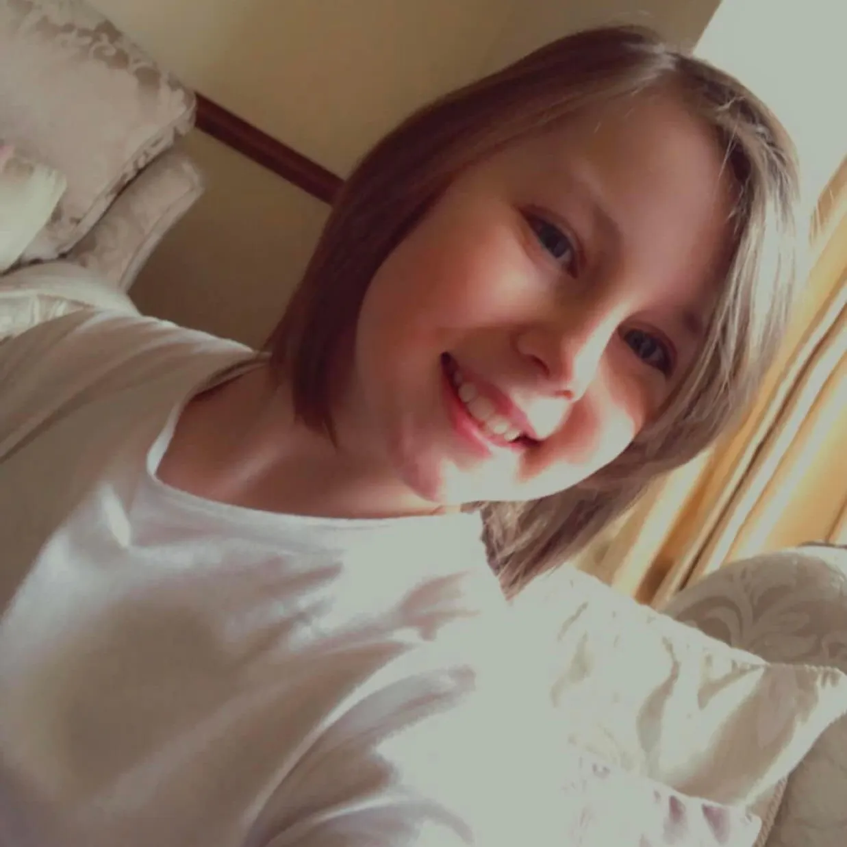 Eve smiling at the camera, take a selfie. In a shite t-shirt with shoulder length brown hair