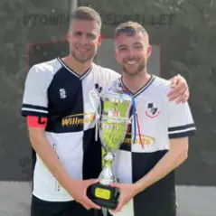 2 male football players win black and white football shirts checks, side by side, holding a silver trophy, one payer with arm around the other