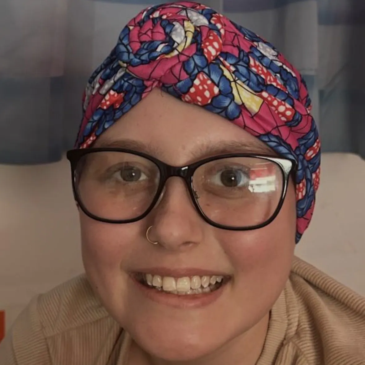 Leya smiling at the camera, wearing black rimmed glasses and a colourful headscarf