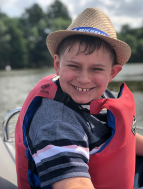 Joshua sat on a boat wearing a life jacket and hat, big smile on his face