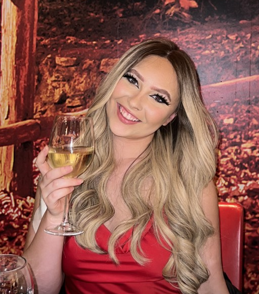 Eloise sitting and smiling at the camera with a glass of wine in hand