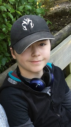 Alex smiling at the camera, headphones around his neck and a baseball cap on head
