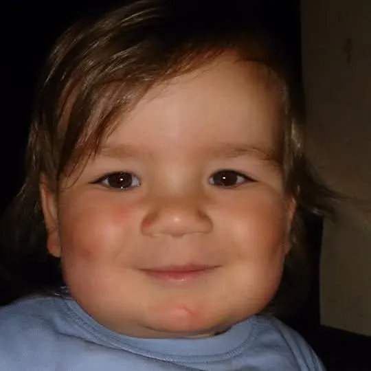 Nathan smiling at the camera with a light blue top on with a monkey head and the words play time.