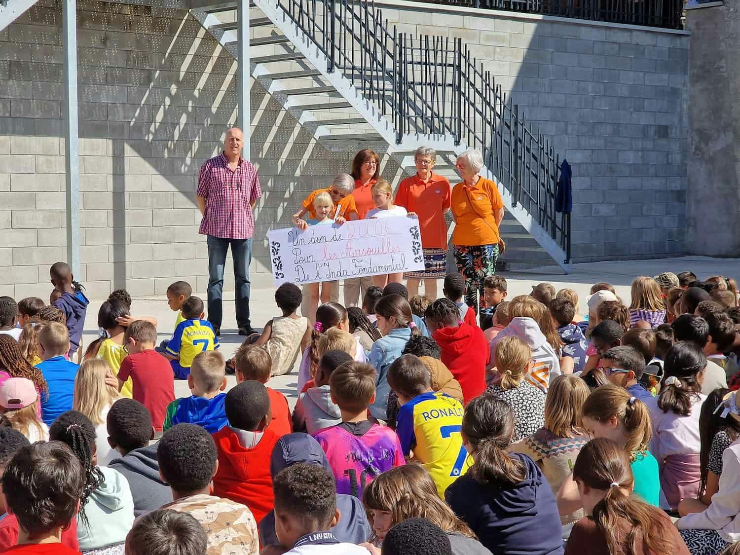 Élèves et équipe pédagogique montrant un don de 2000€ pour les Arsouilles de l'Inda fondamentale.
