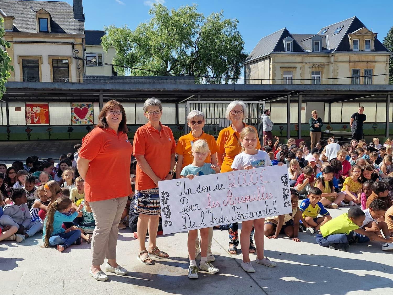 Élèves et équipe pédagogique montrant un don de 2000€ pour les Arsouilles de l'Inda fondamentale.