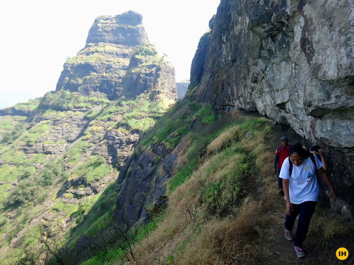 AMK Trek - Trekkers walking on the ledge with Madangad in the background - Indiahikes - Nitesh Kumar