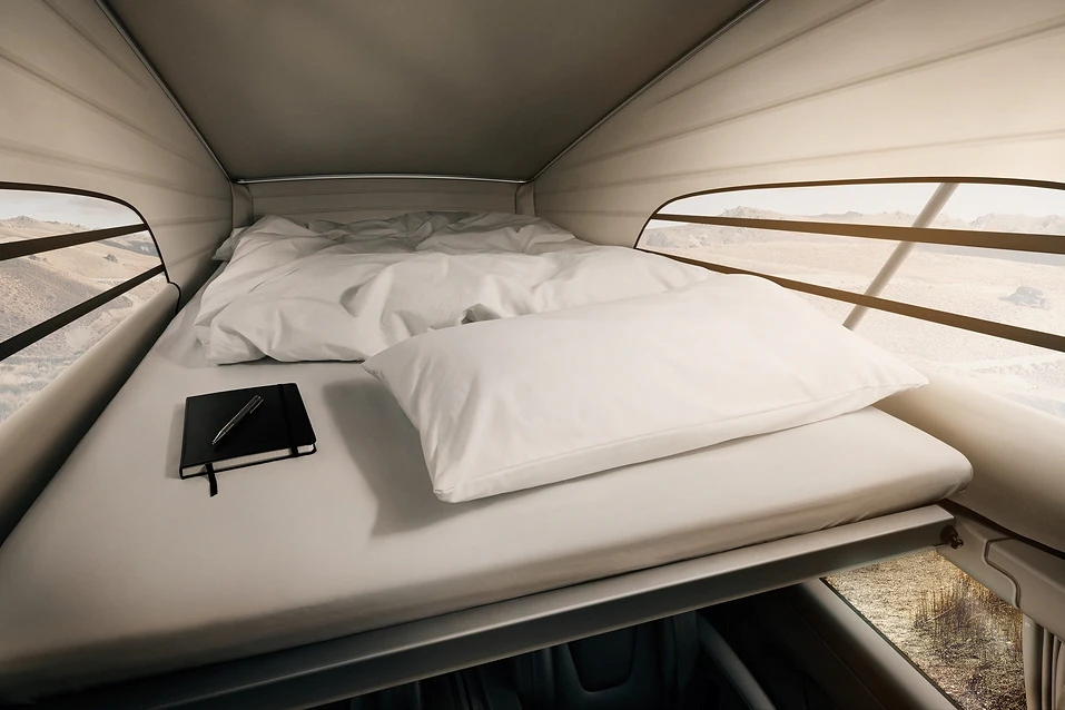Interior view of a campervan bed with white bedding, pillow, notebook, and pen near a panoramic window.