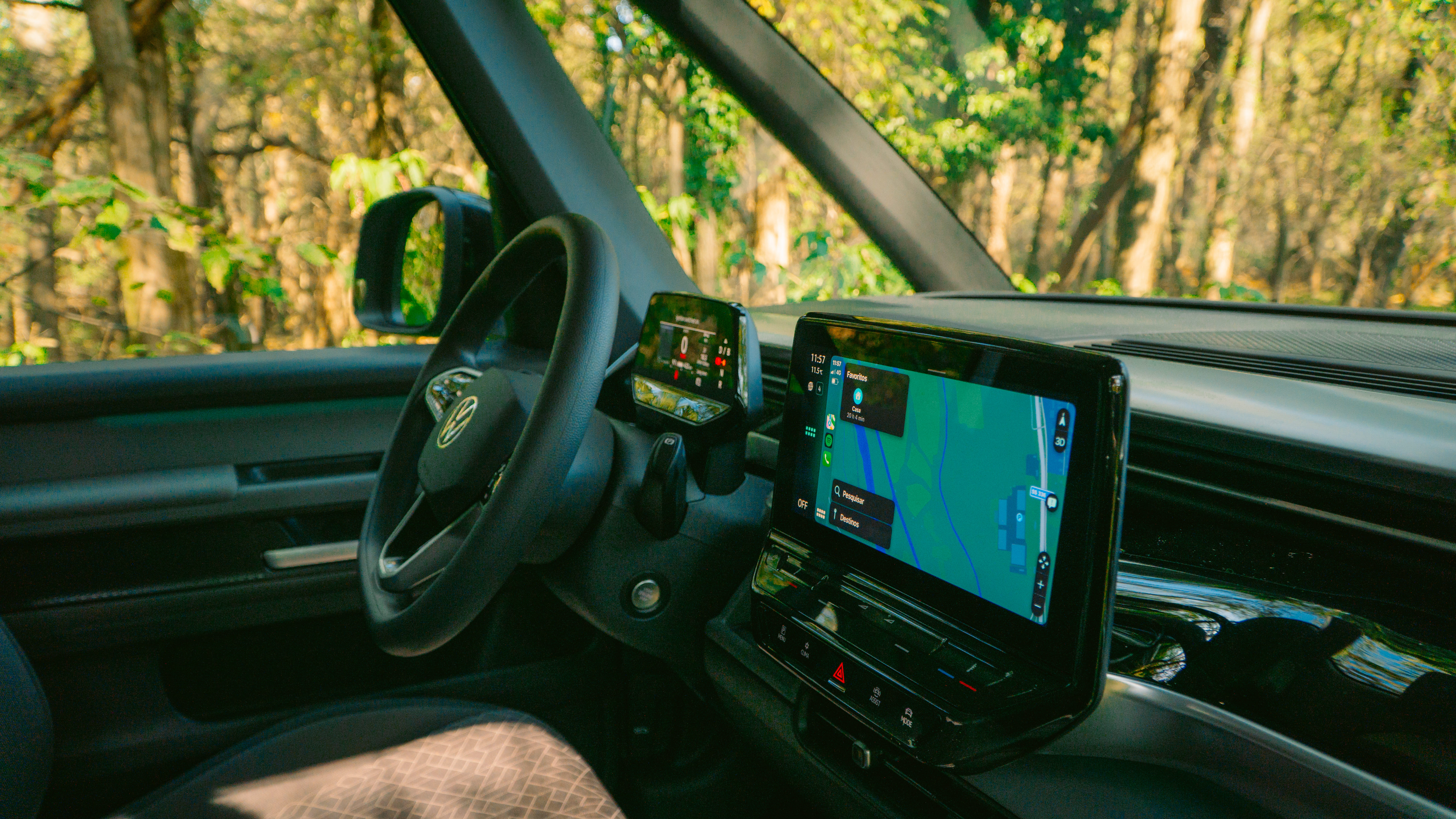 Modern camper van dashboard with digital navigation screens, steering wheel, and forest scenery visible through the windows.
