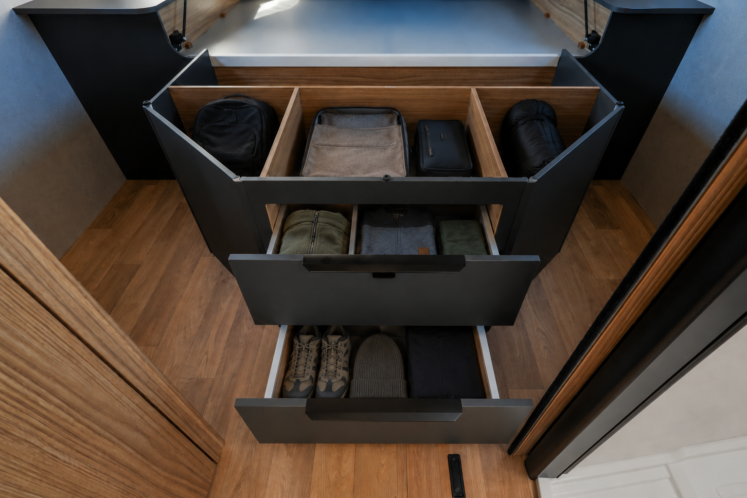 Van interior with open storage drawers and compartments, wooden floor, various bags and accessories neatly organized.