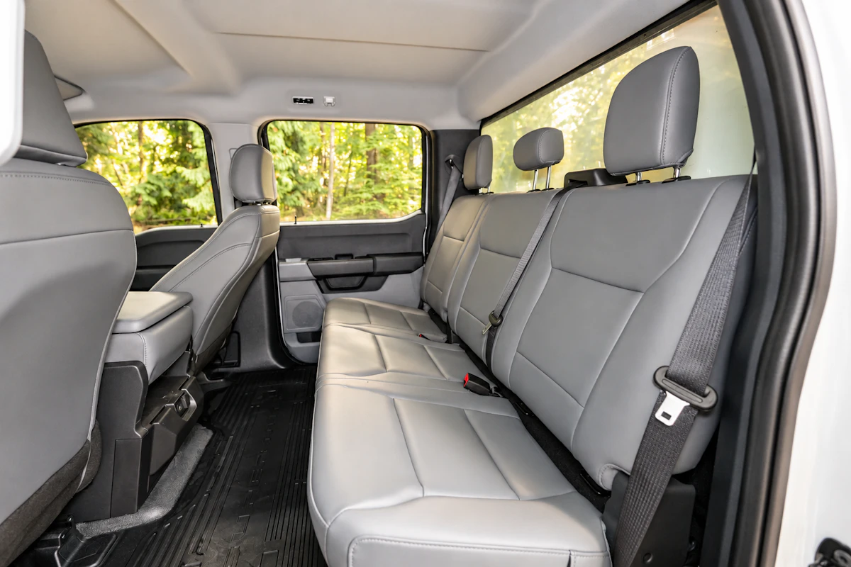 Van interior with three rear seats, grey upholstery, visible seatbelts, and front seats partially visible.