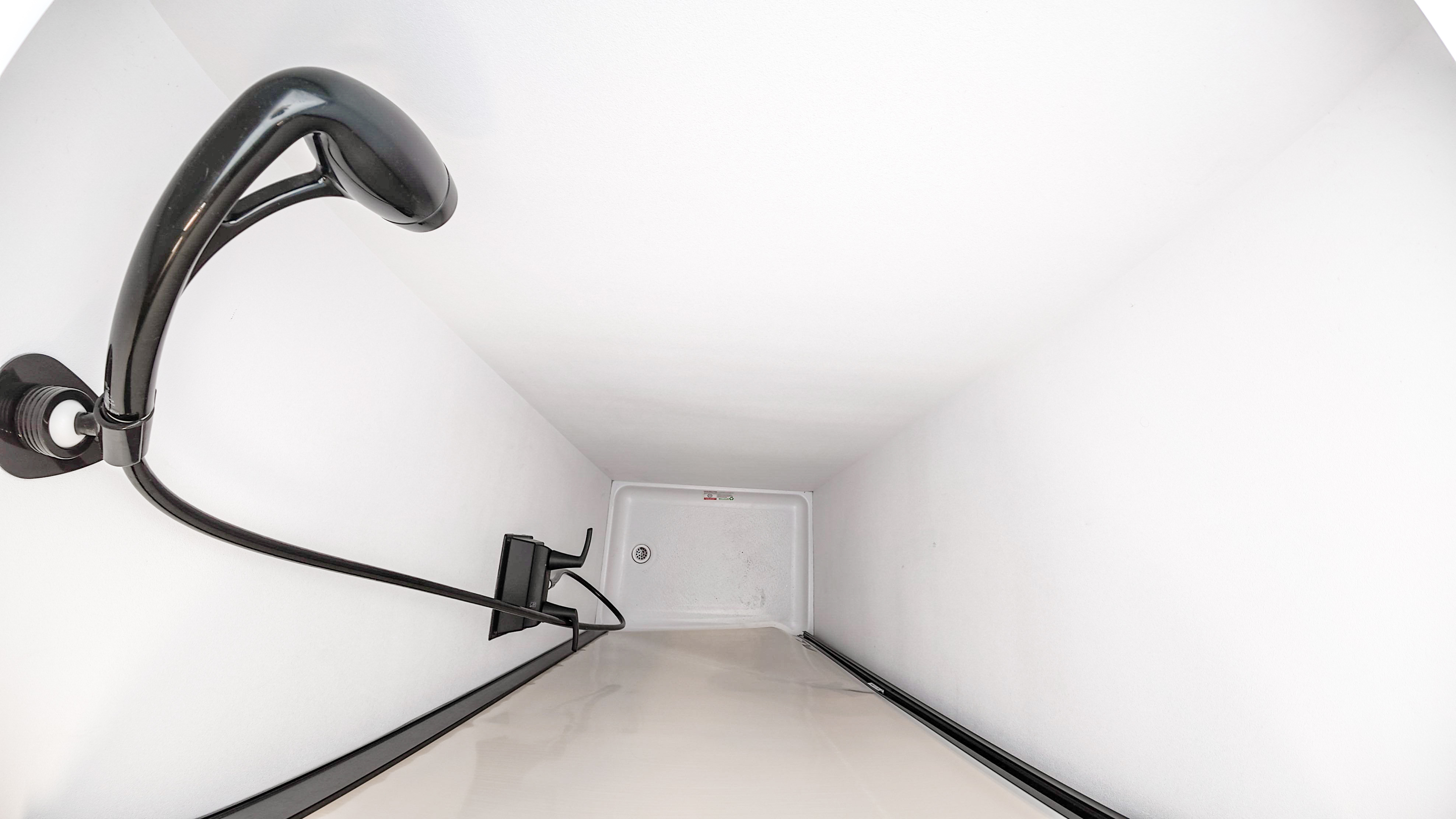 Van interior shower cubicle with handheld shower head, white walls, and a drain in the floor.