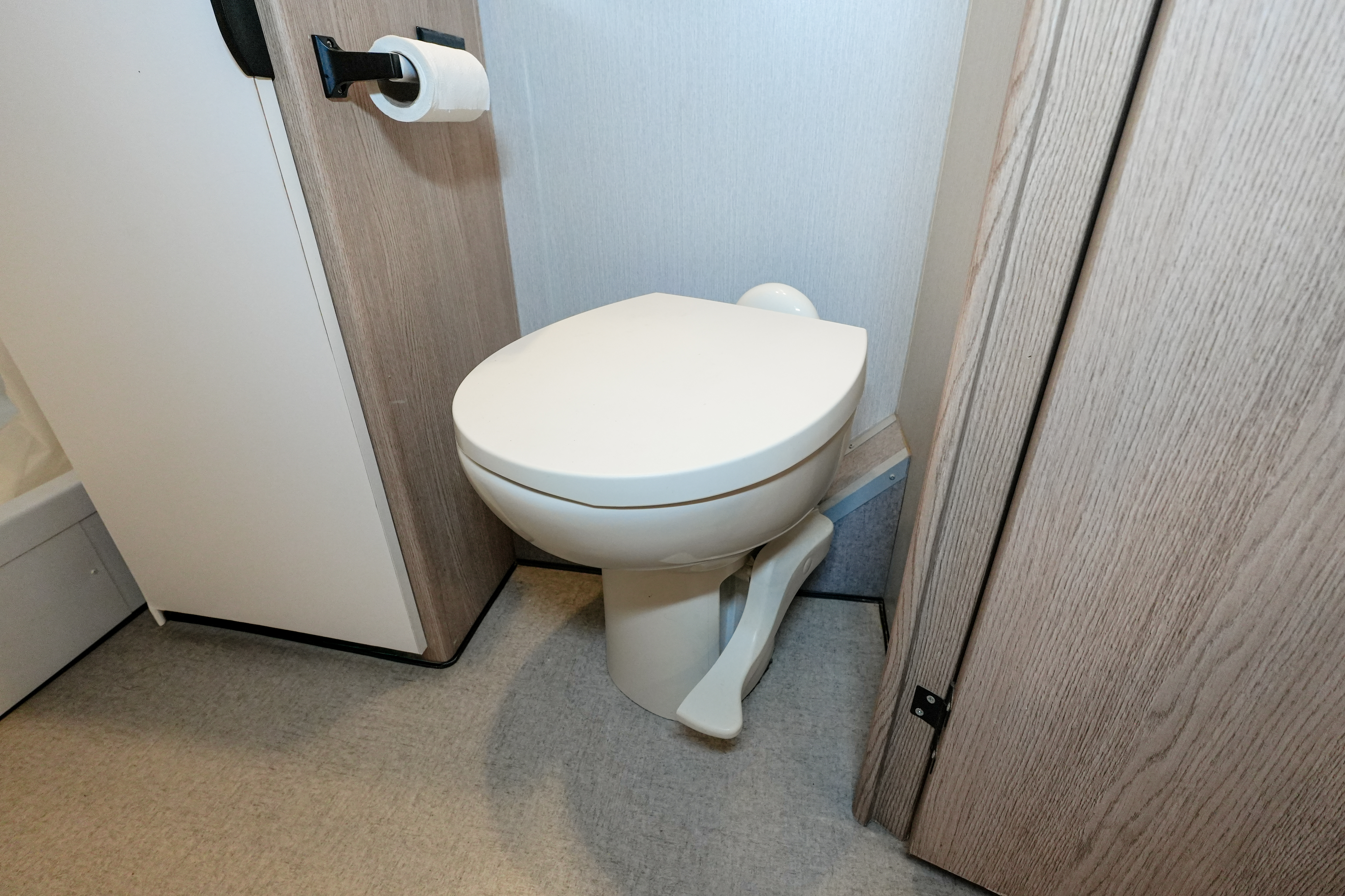 Small bathroom area with a toilet, toilet paper holder, and light wood paneling inside the van.