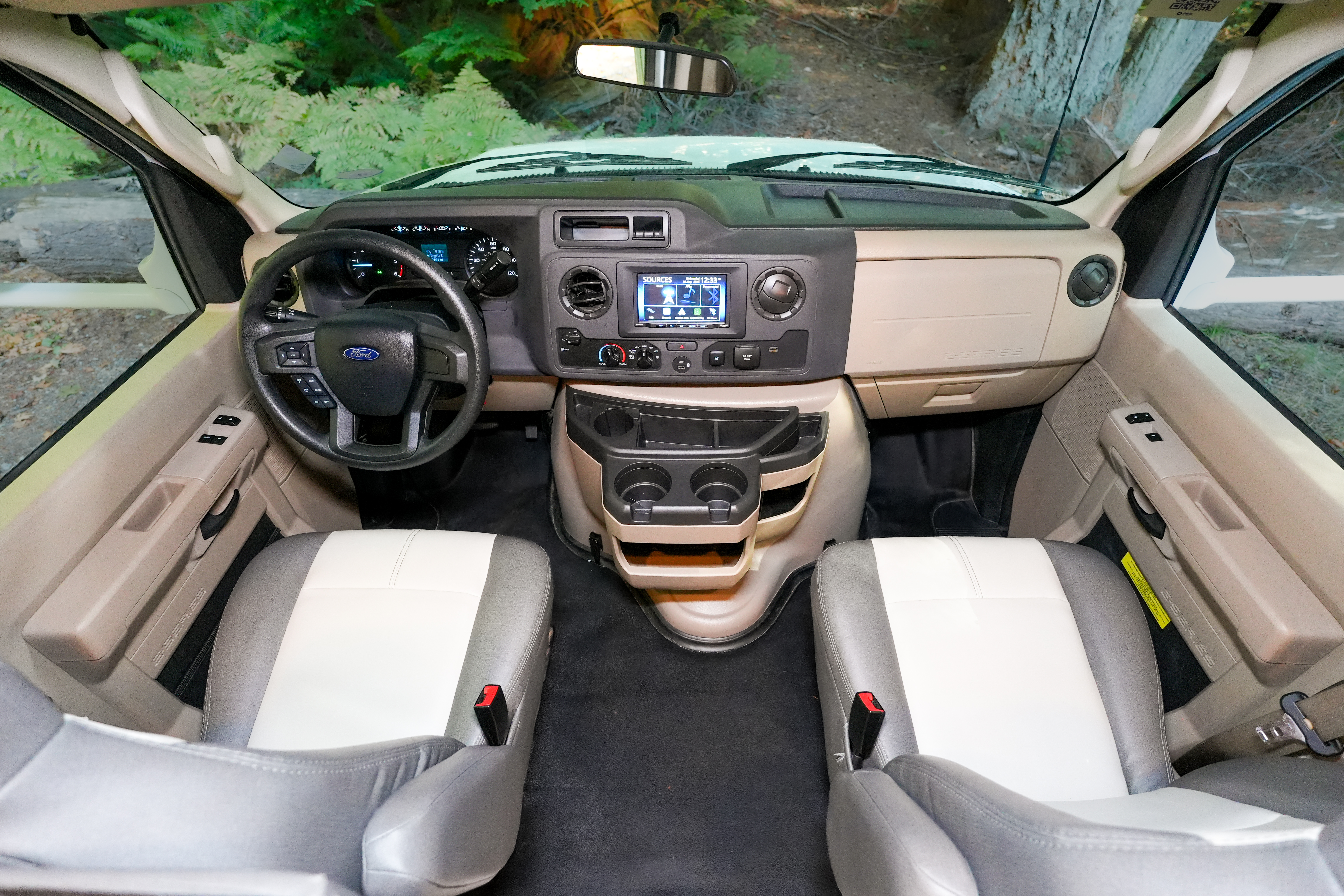Front view of van interior cockpit with two seats, dashboard, steering wheel, and central console controls visible.