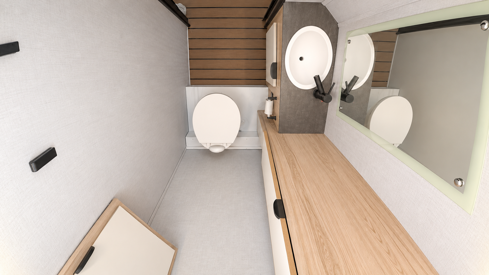 Van interior with toilet, sink, large mirror, wooden countertop, cabinet, and white walls.