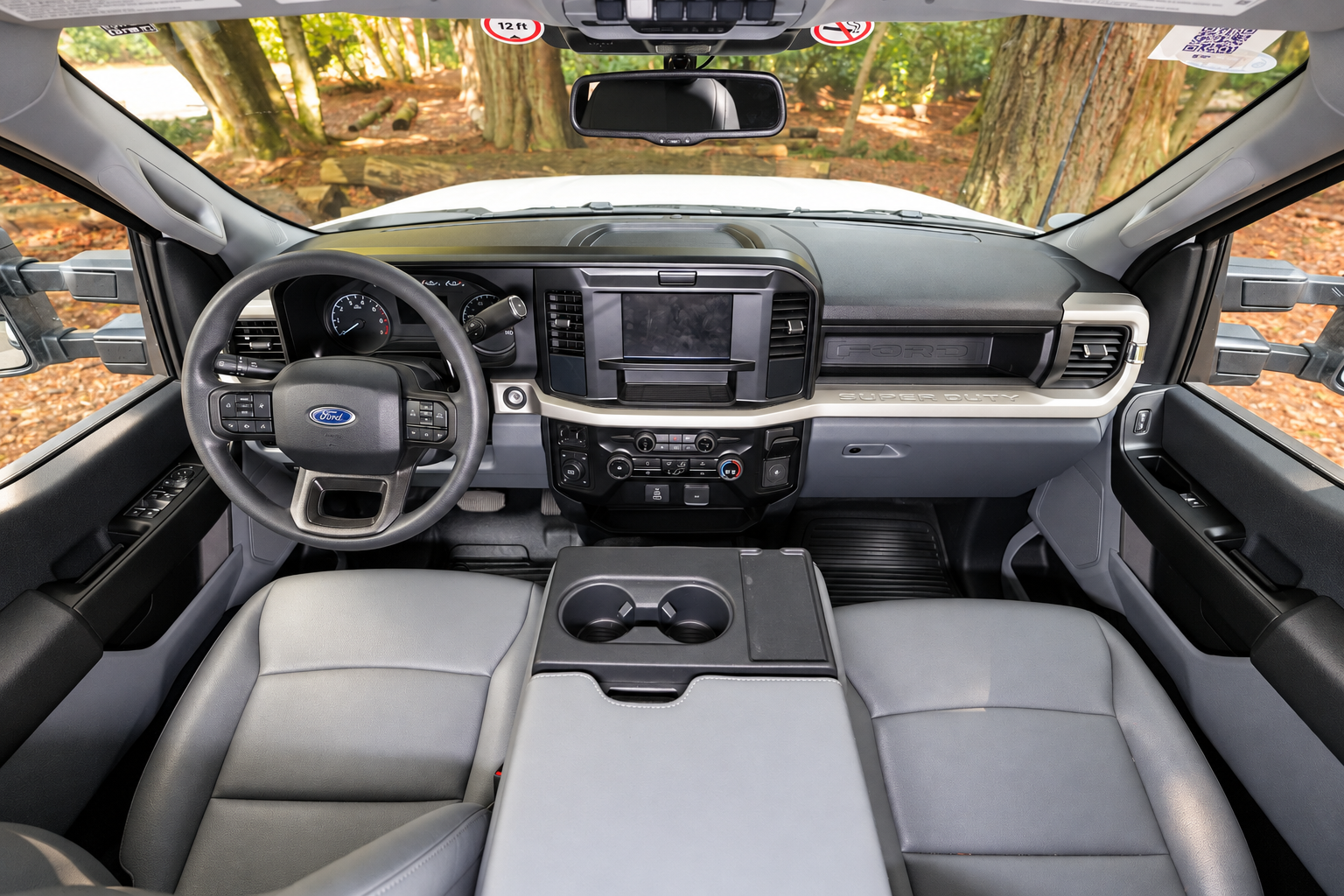 Front cabin view showing dashboard, steering wheel, touchscreen, cup holders, and two front seats in a van.