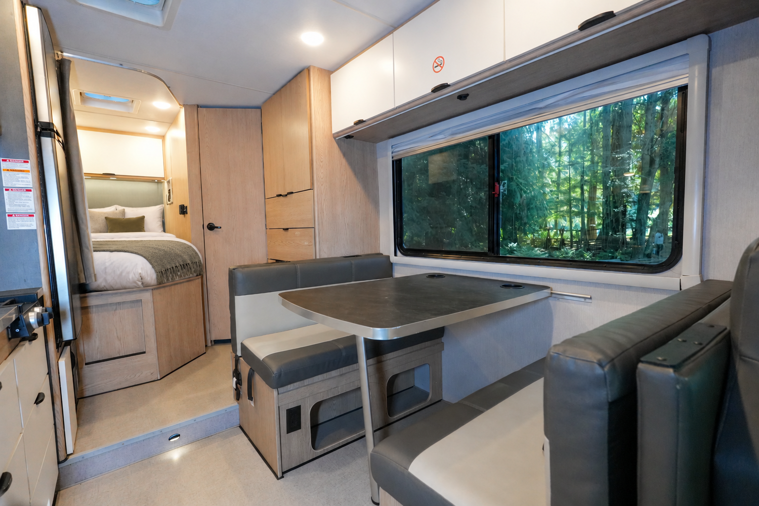 Interior view showing dining area, table, benches, bed in rear, cabinets, and large side window inside the van.