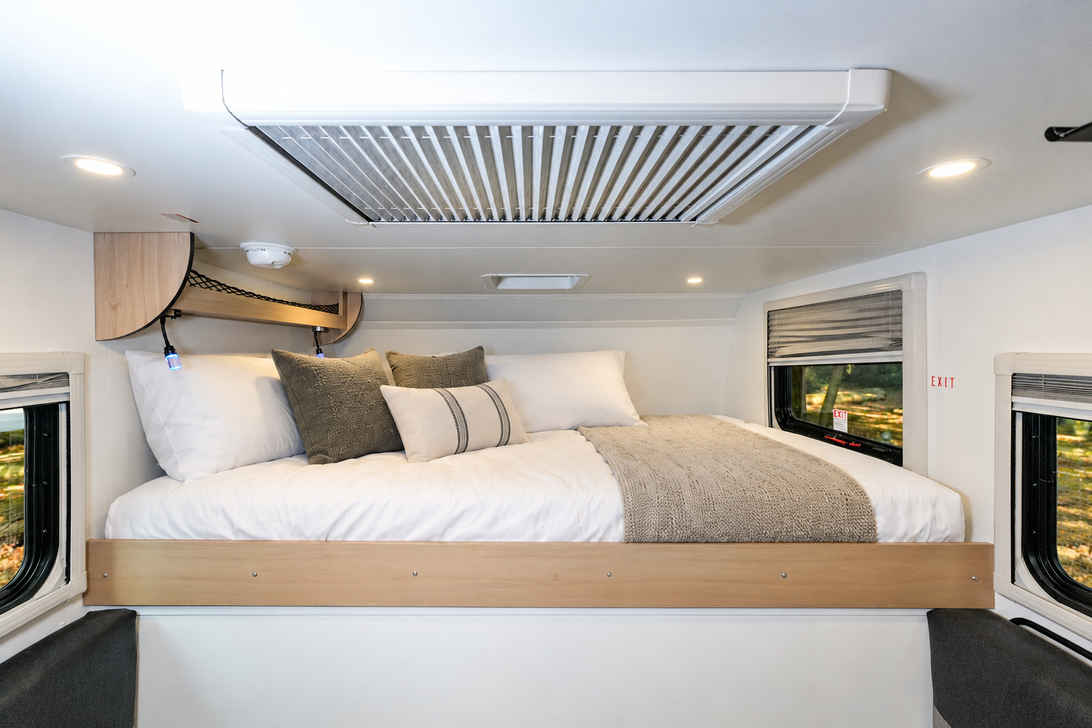 Interior view showing raised double bed, storage shelf, windows with blinds, and ceiling ventilation in the van.