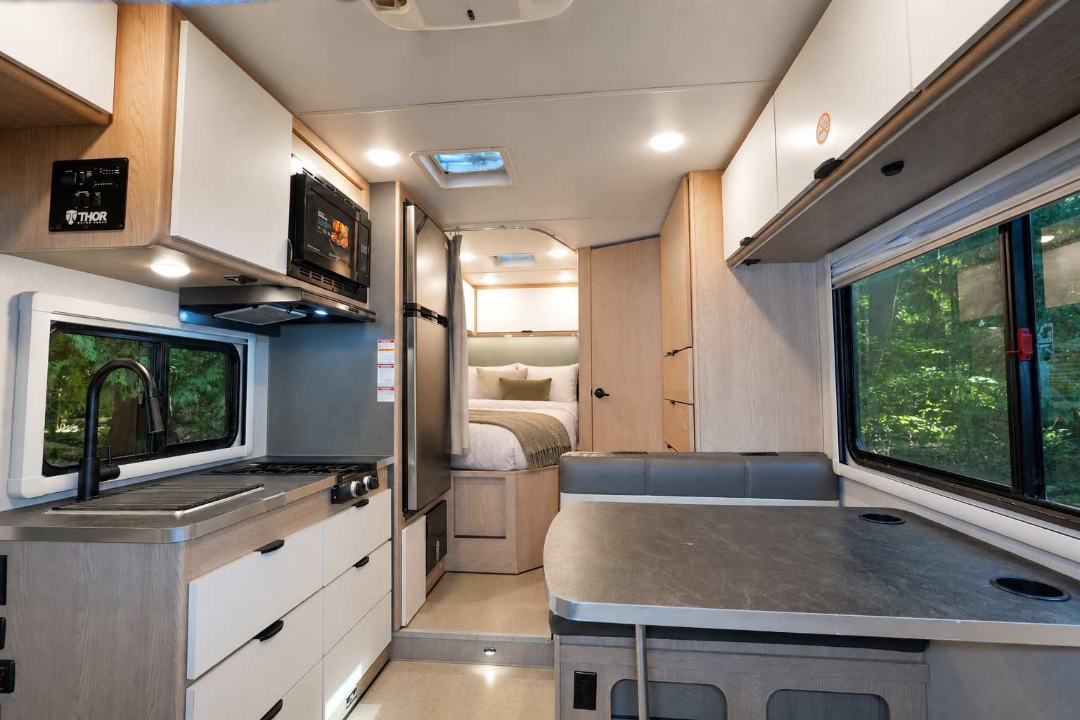 Kitchen, dining area, and bed inside van with cabinets, sink, stove, microwave, windows, and seating visible.
