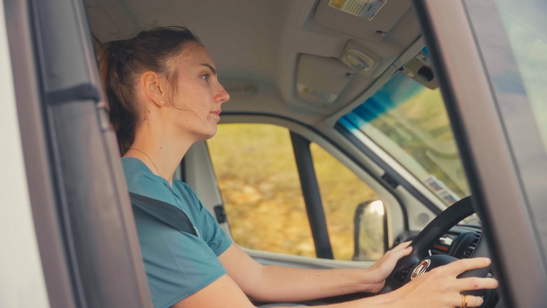 Woman driving a campervan, focused on the road, with natural scenery visible through the window.
