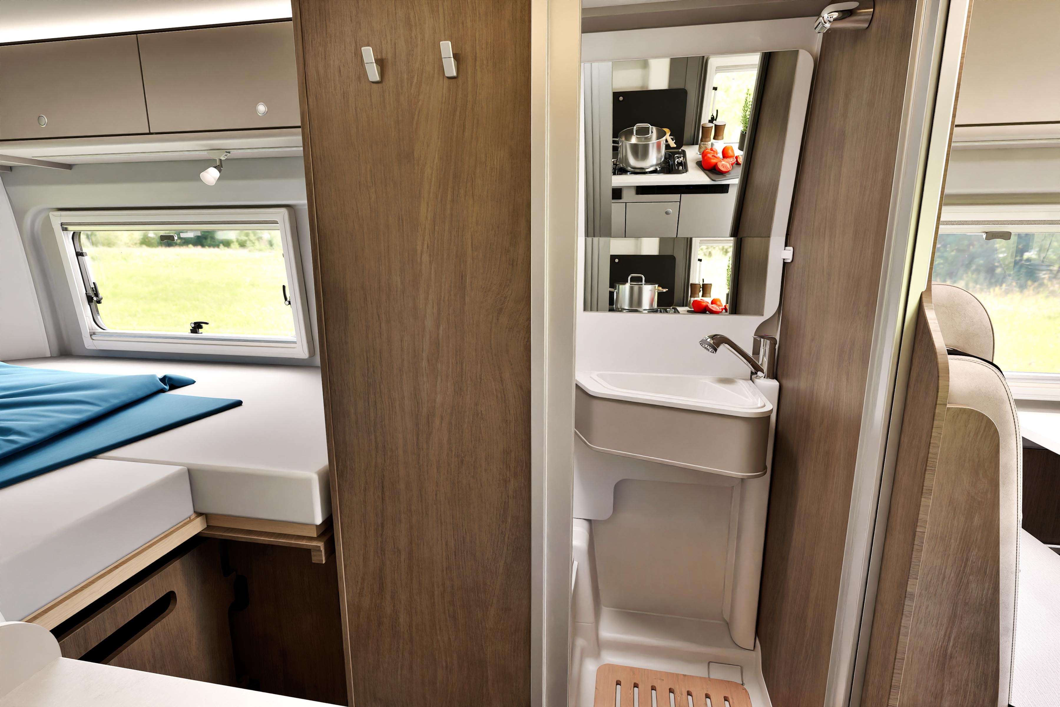 Interior view of a campervan with bed, bathroom sink, mirror, shelves, and large windows with outside scenery.
