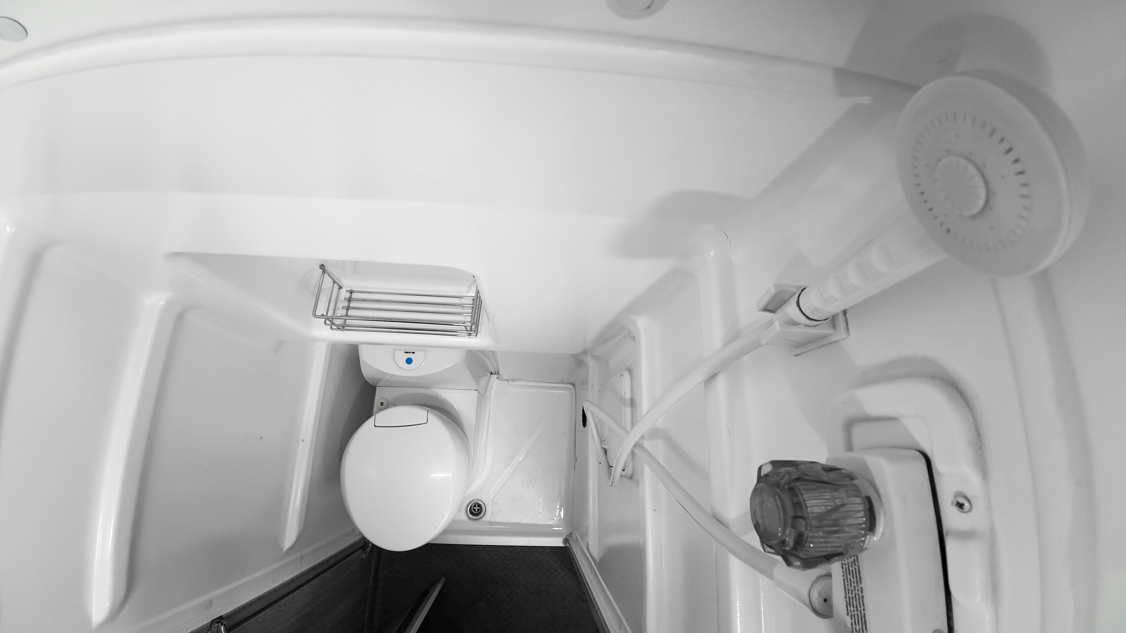 Compact van bathroom with toilet, overhead shower, wall-mounted soap holder, and sink visible in a white interior.