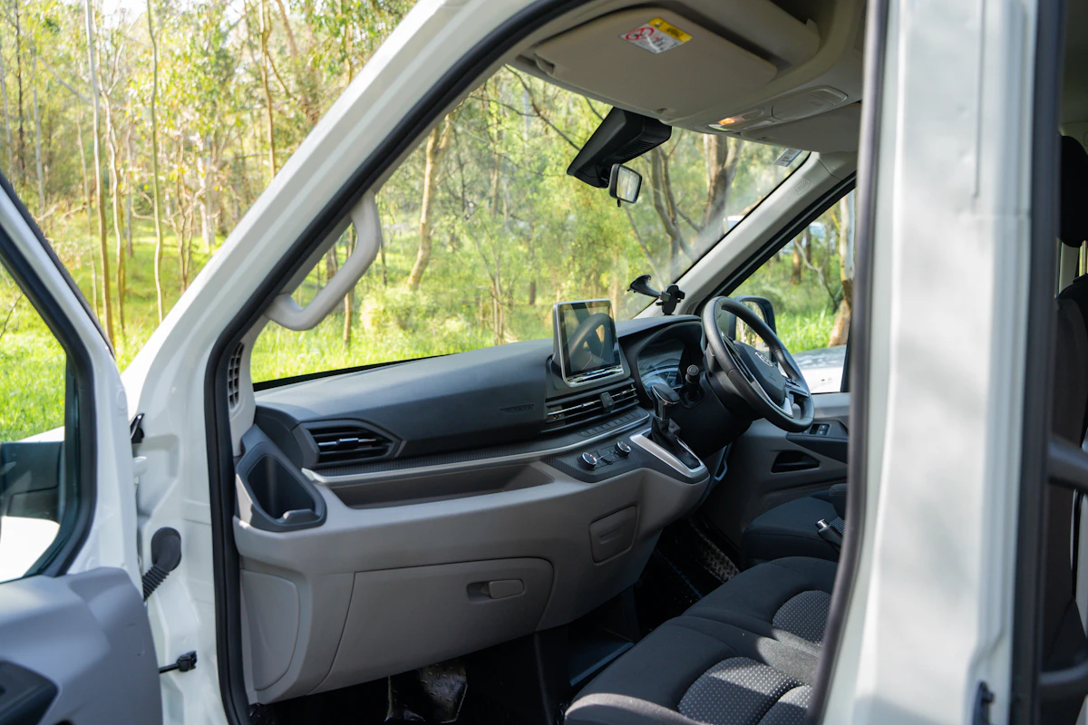 Open campervan driver’s side door showing modern dashboard, touchscreen display, and front seats with forest background.
