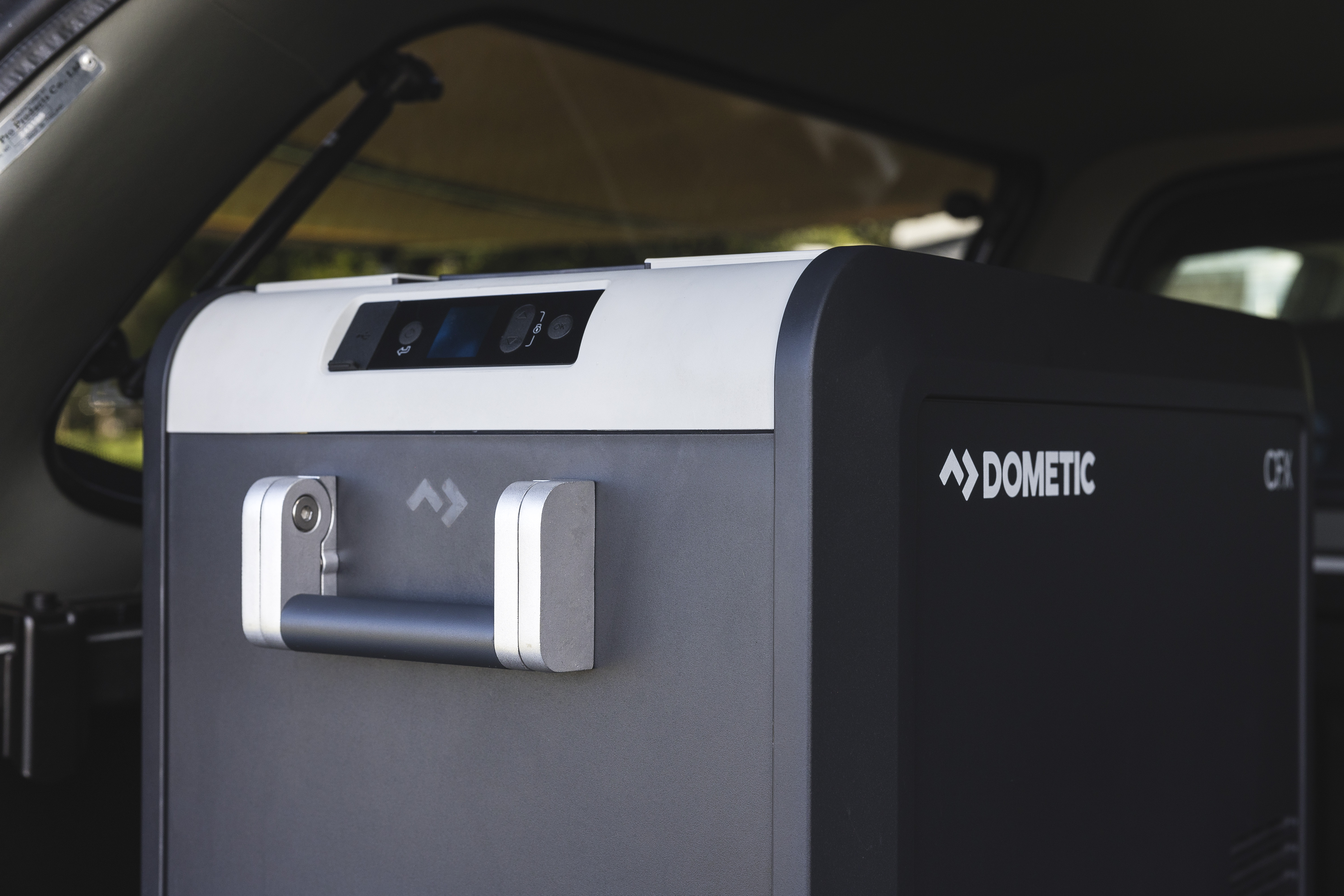 Portable Dometic camping fridge with handle, placed inside a campervan, suitable for travel and outdoor adventures.