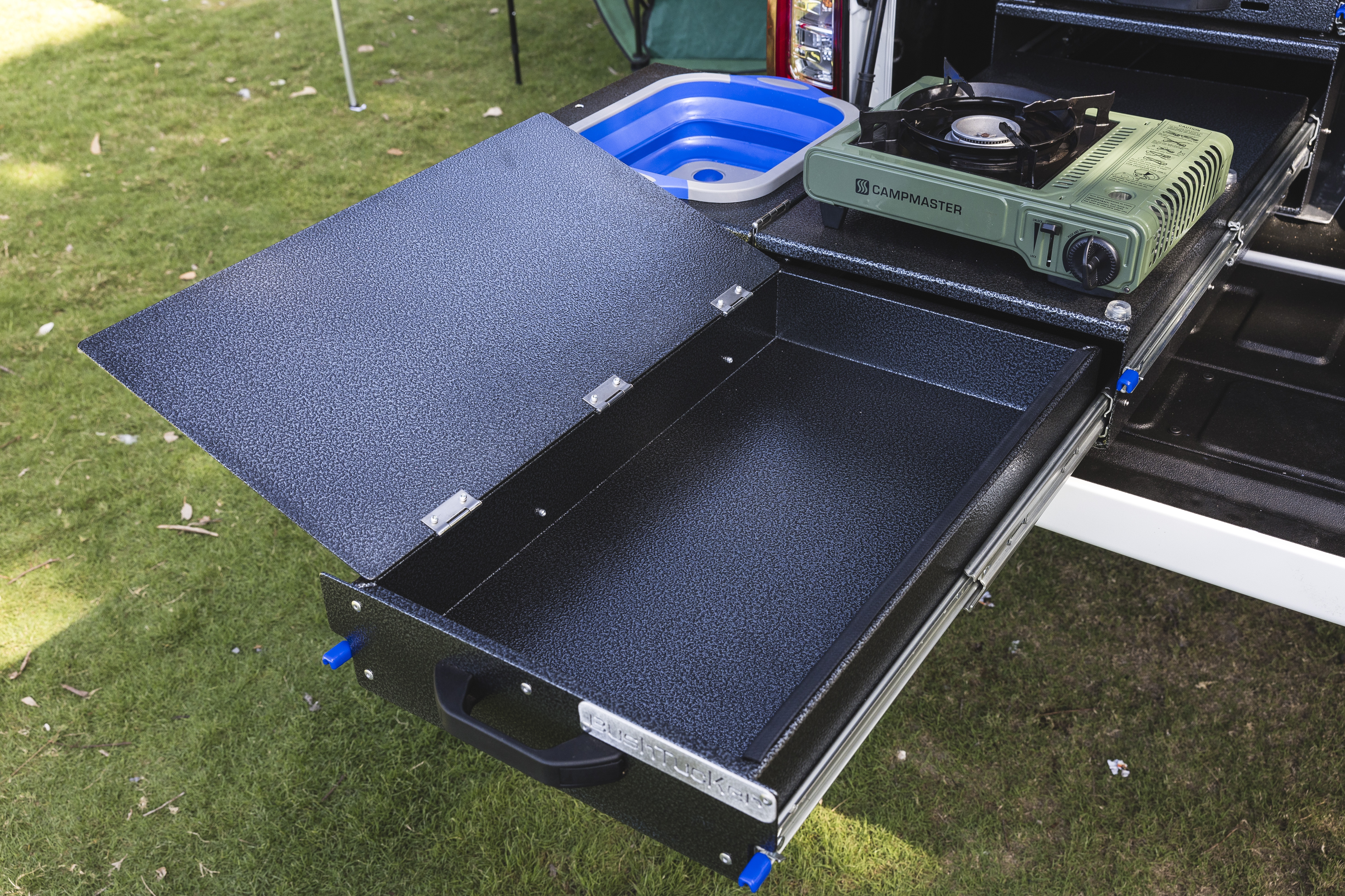 Pull-out campervan kitchen drawer with stove and open storage compartment, set up outdoors on grass.