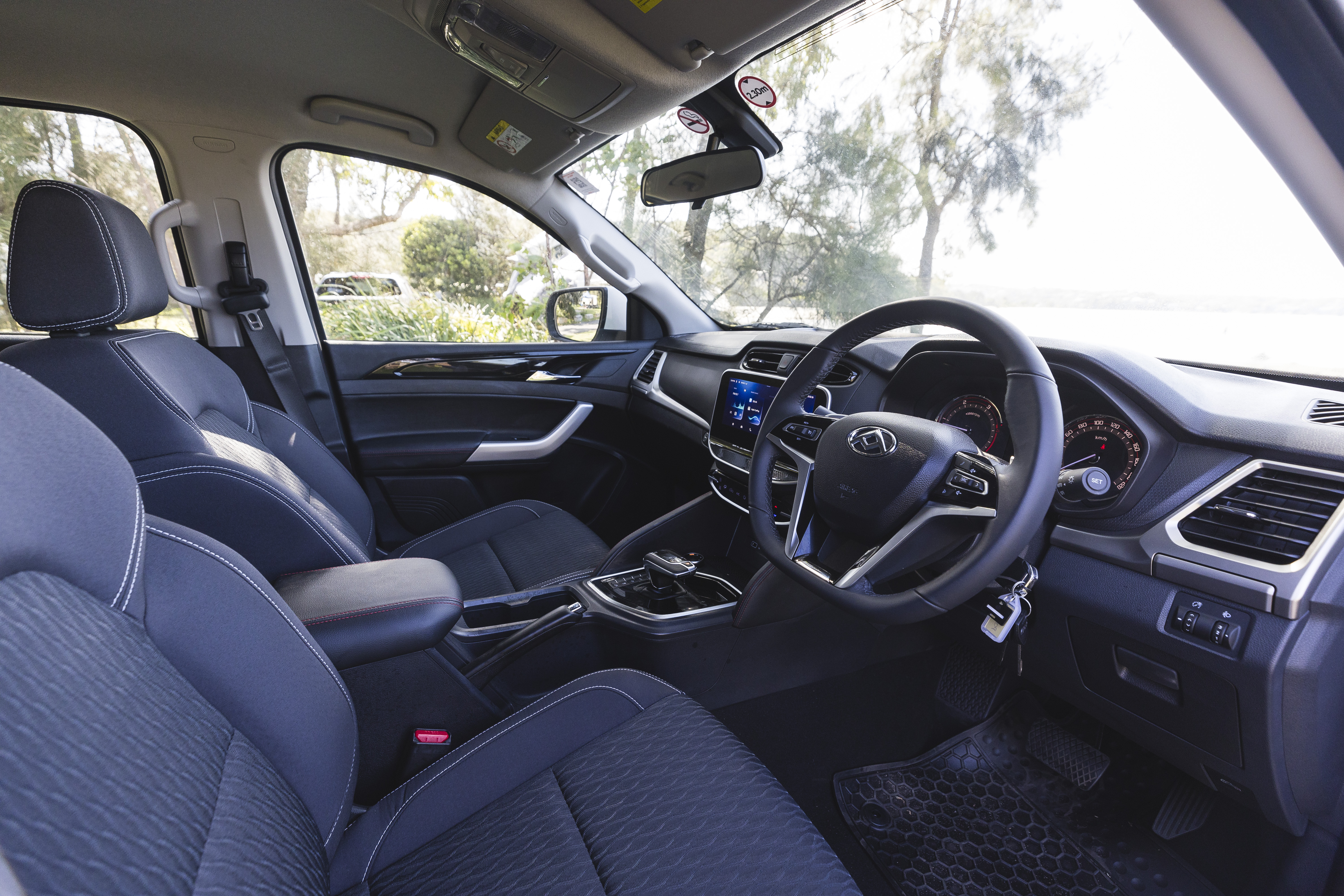 Modern campervan interior featuring front seats, steering wheel, dashboard, and centre console with natural light through windows.