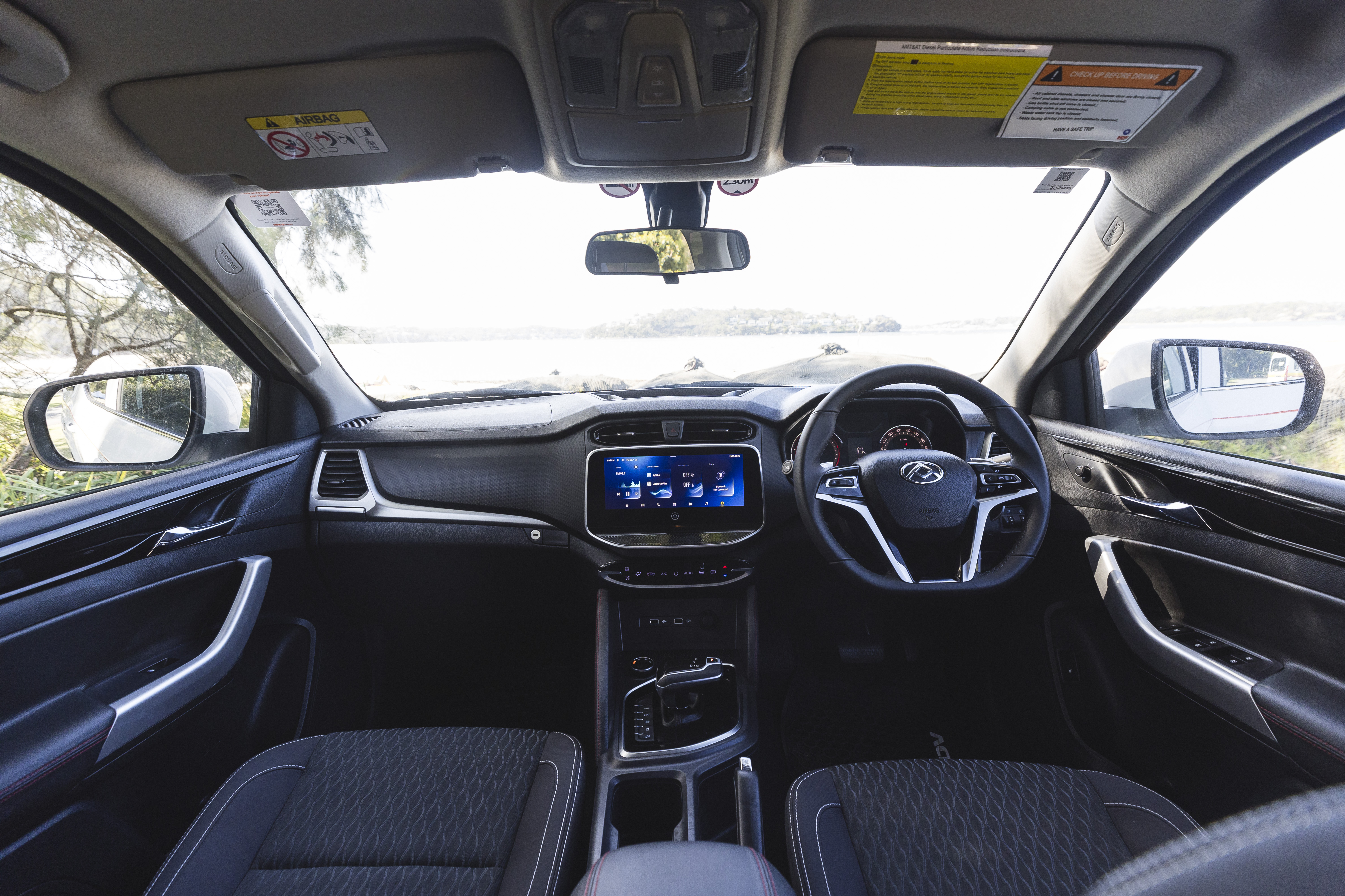 Modern campervan interior with two front seats, touchscreen dashboard, steering wheel, and wide windows facing a scenic view.