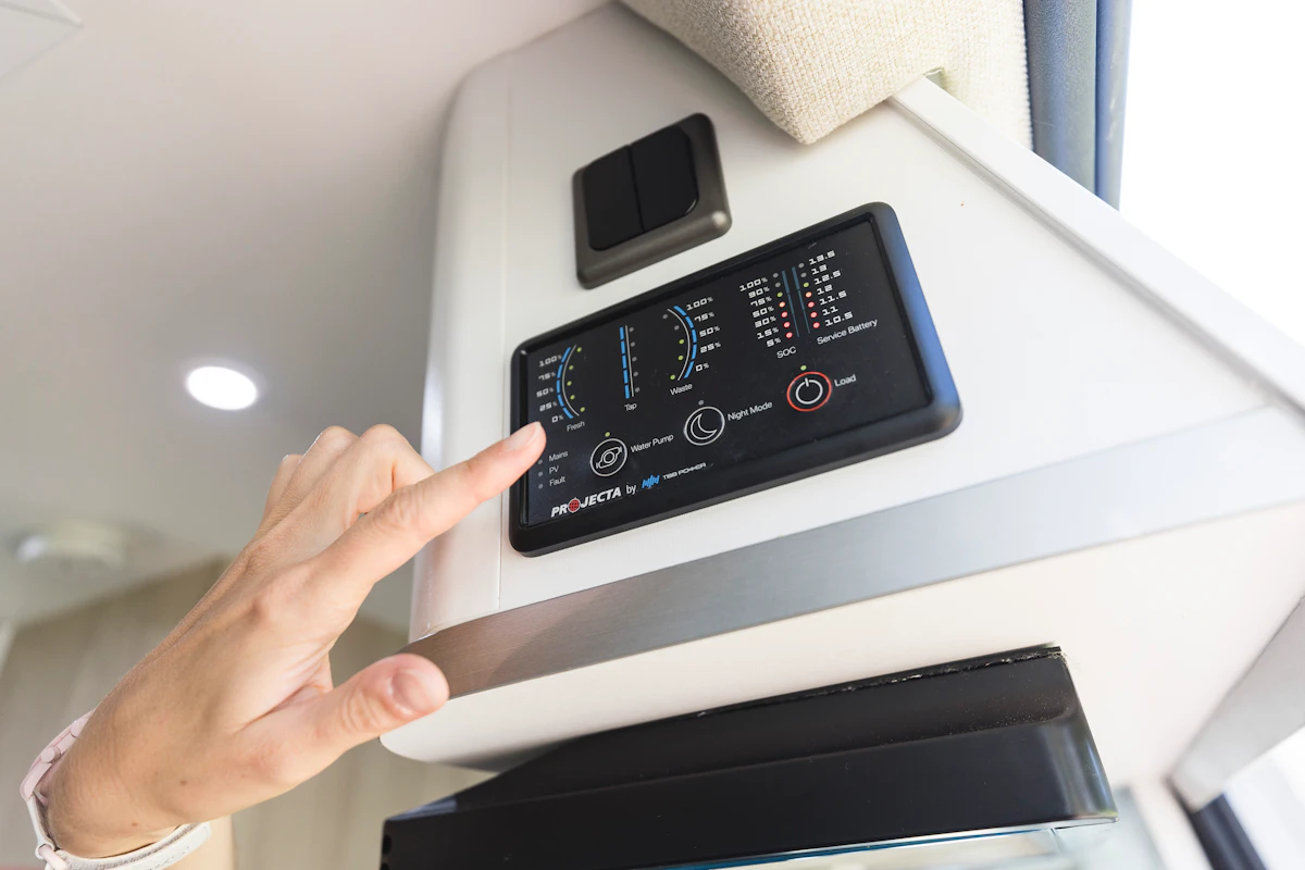 Hand adjusting control panel inside a camper van, displaying gauges and indicators for vehicle systems.
