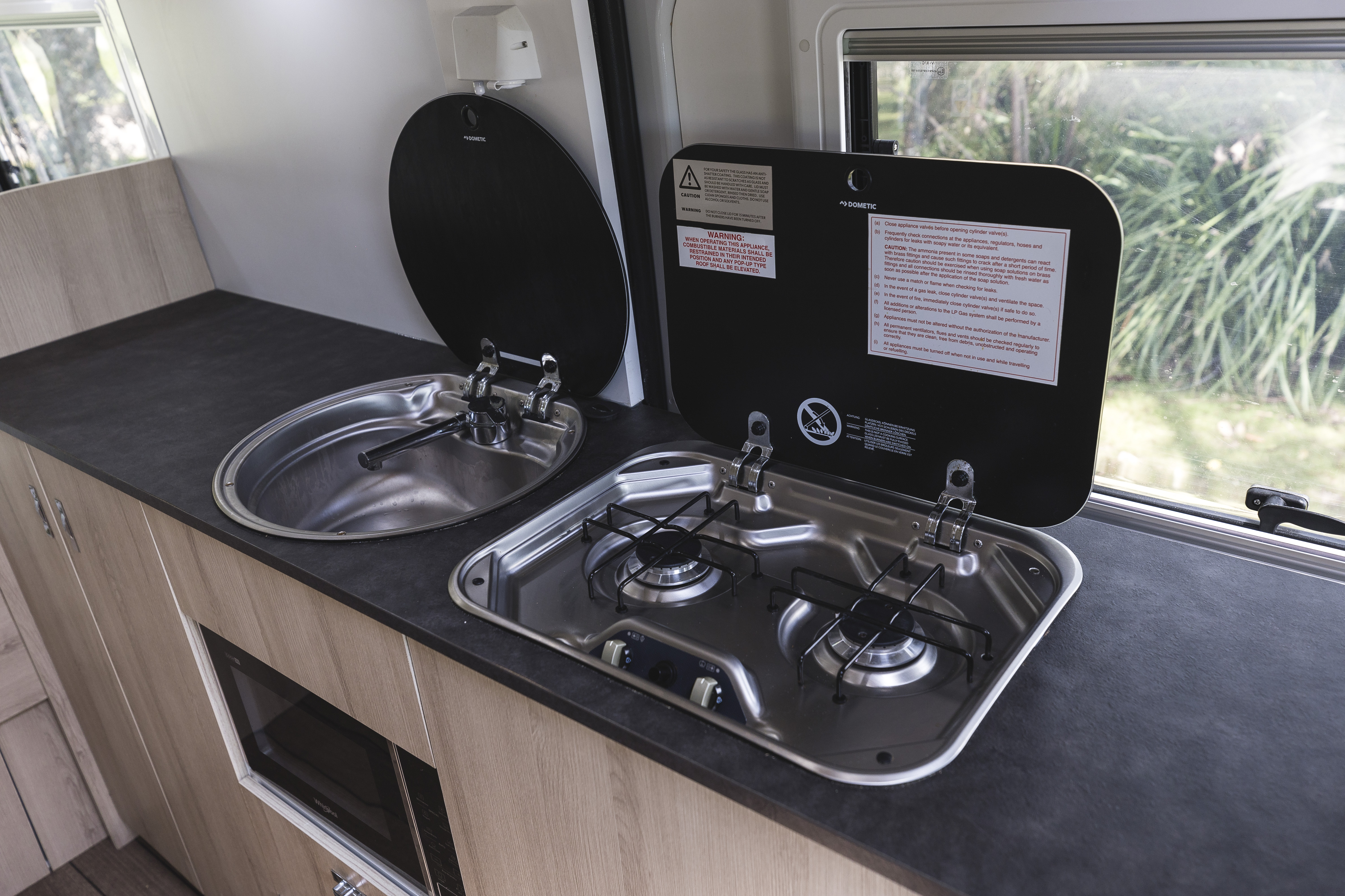 Campervan kitchen with a stainless steel sink and two-burner gas stove, set on a black countertop.