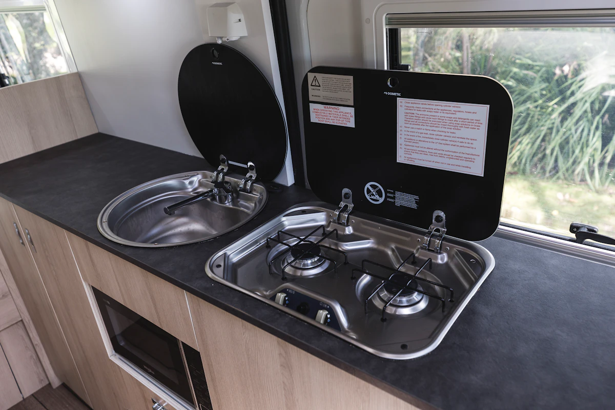 Campervan kitchen with a stainless steel sink and two-burner gas stove, set on a black countertop.