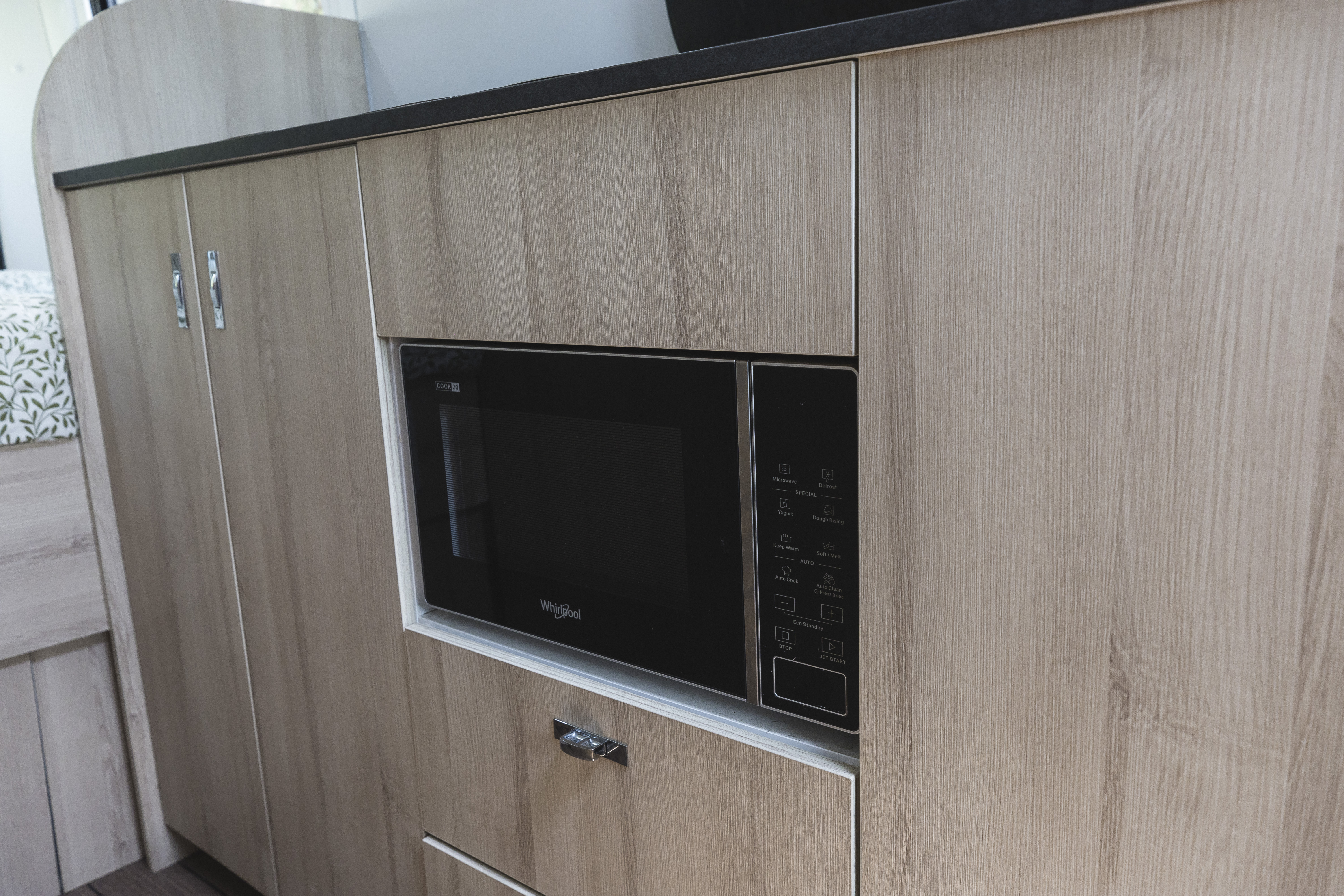 Built-in black microwave oven set in light wood campervan kitchenette cabinetry.