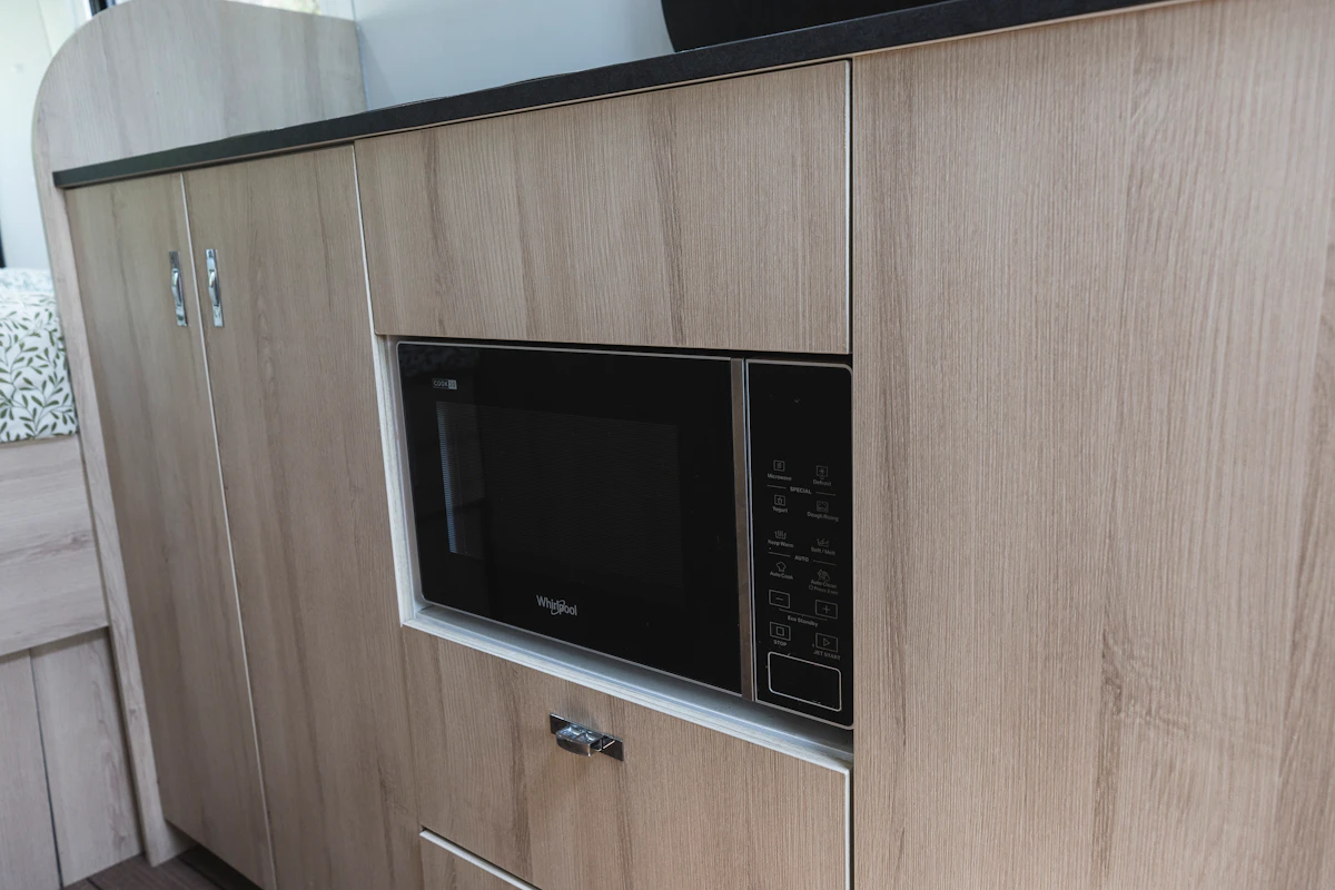 Built-in black microwave oven set in light wood campervan kitchenette cabinetry.