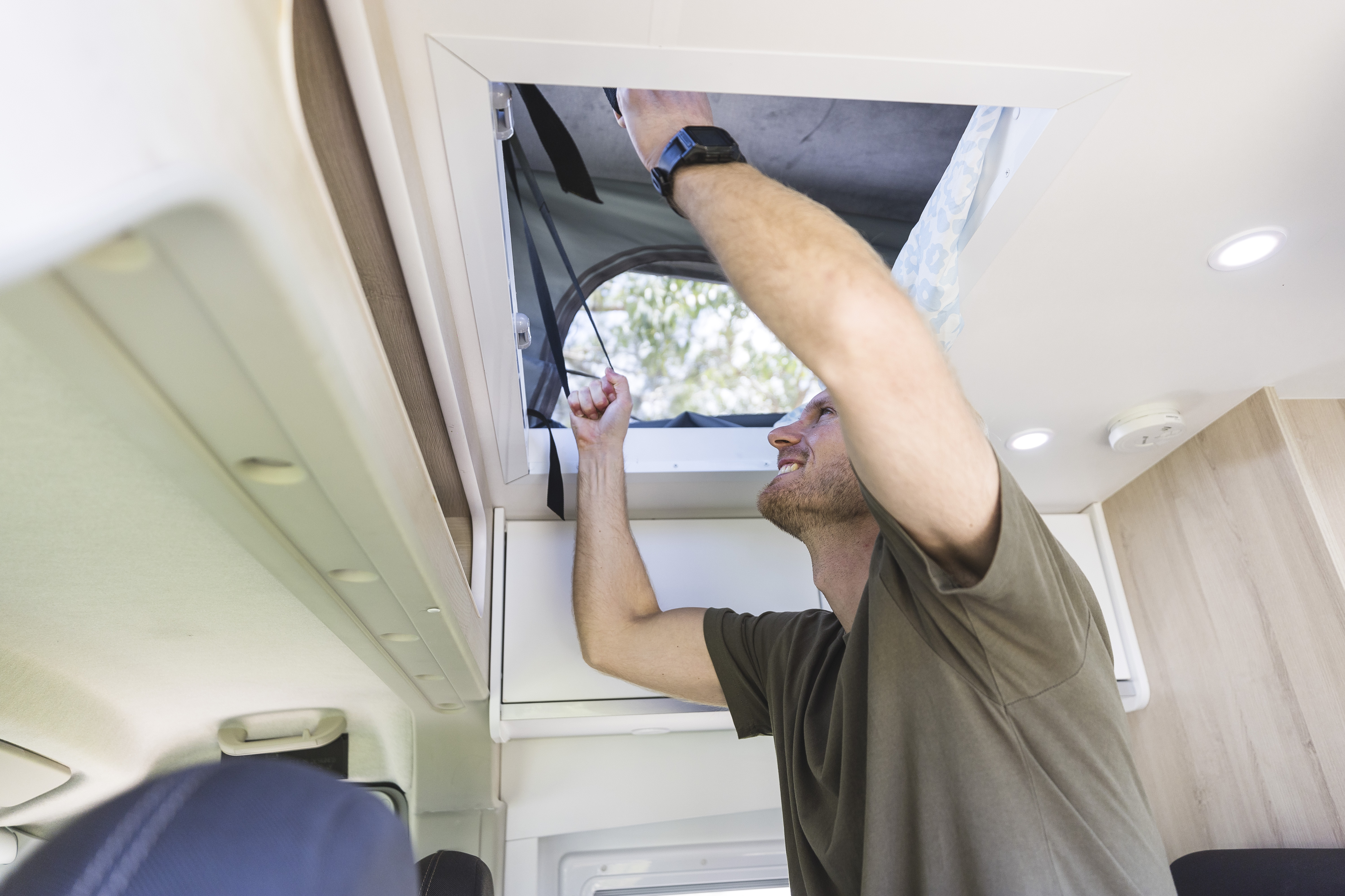 Man opening the roof hatch inside a camper van, letting in light and fresh air.