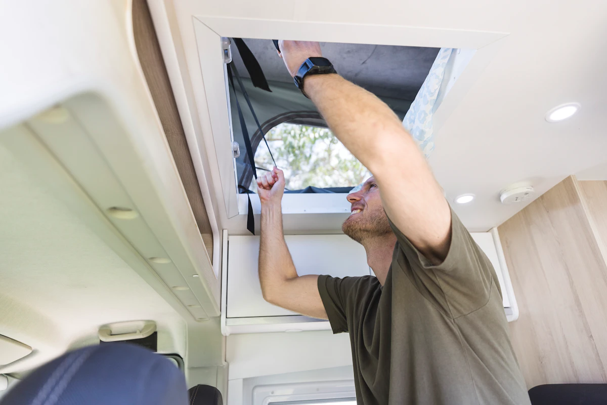 Man opening the roof hatch inside a camper van, letting in light and fresh air.