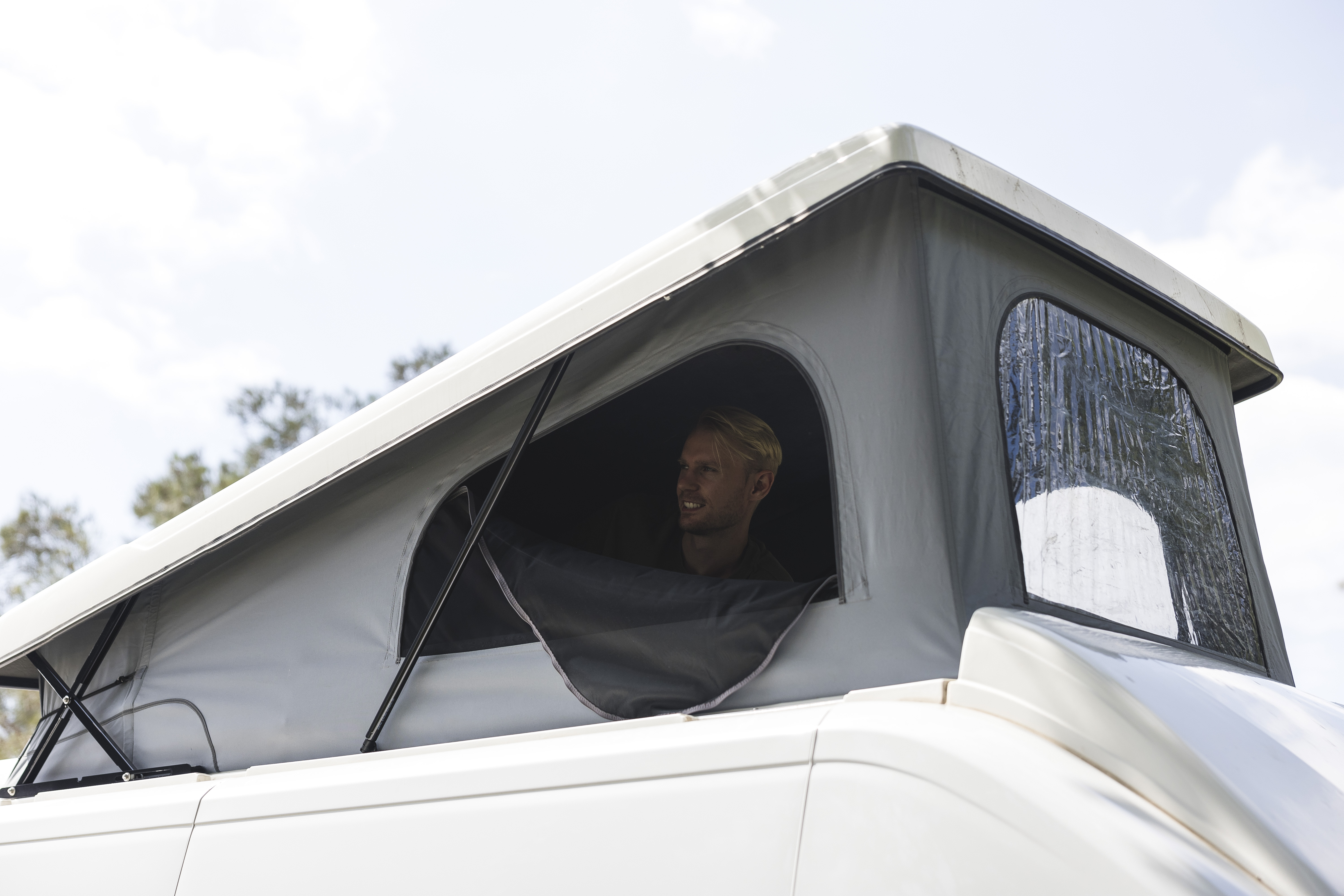 Person sitting inside a raised pop-up roof camper van, looking out through the open side window.
