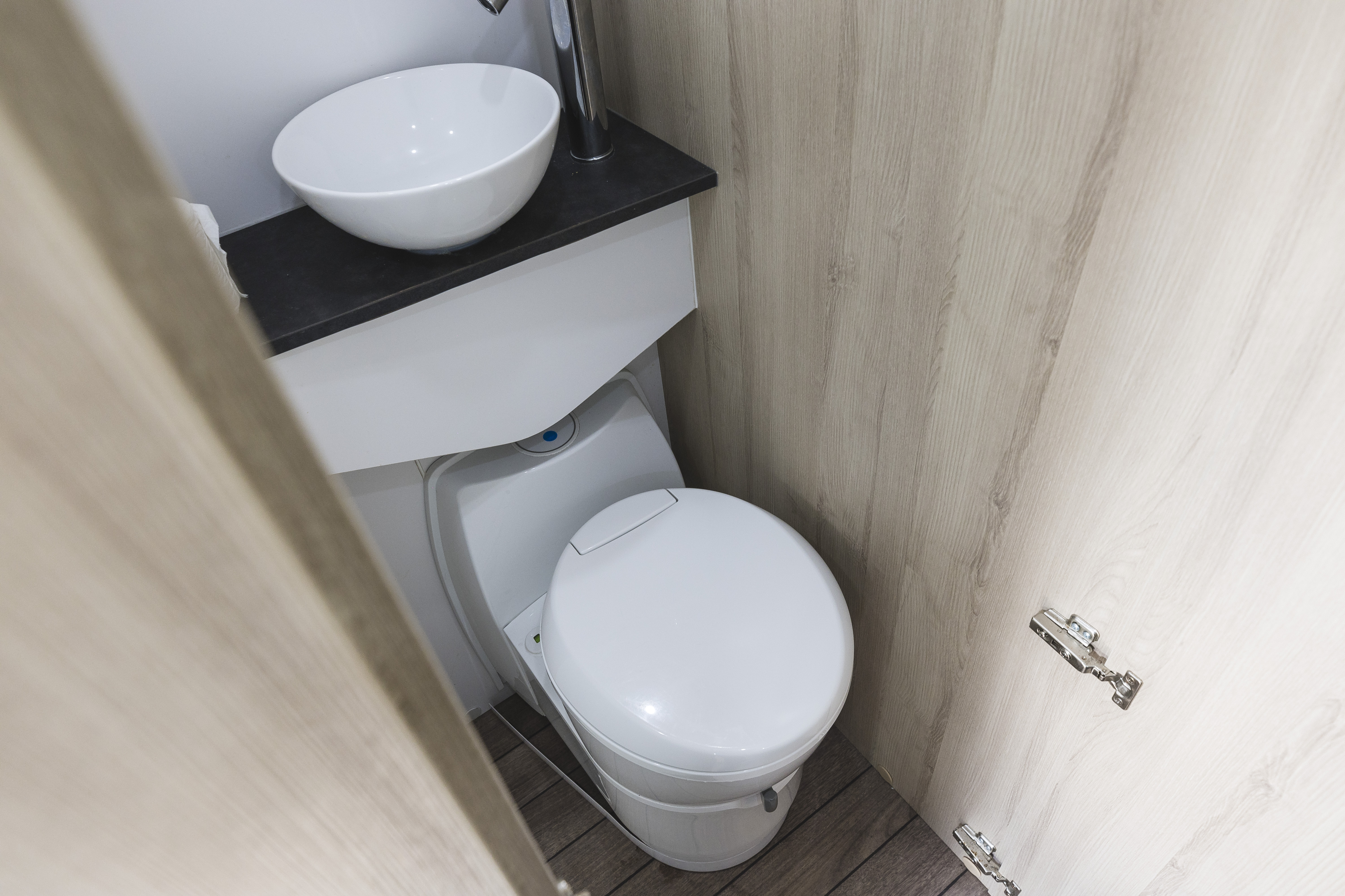 Compact campervan bathroom with a white toilet, modern sink, and light wooden walls and flooring.