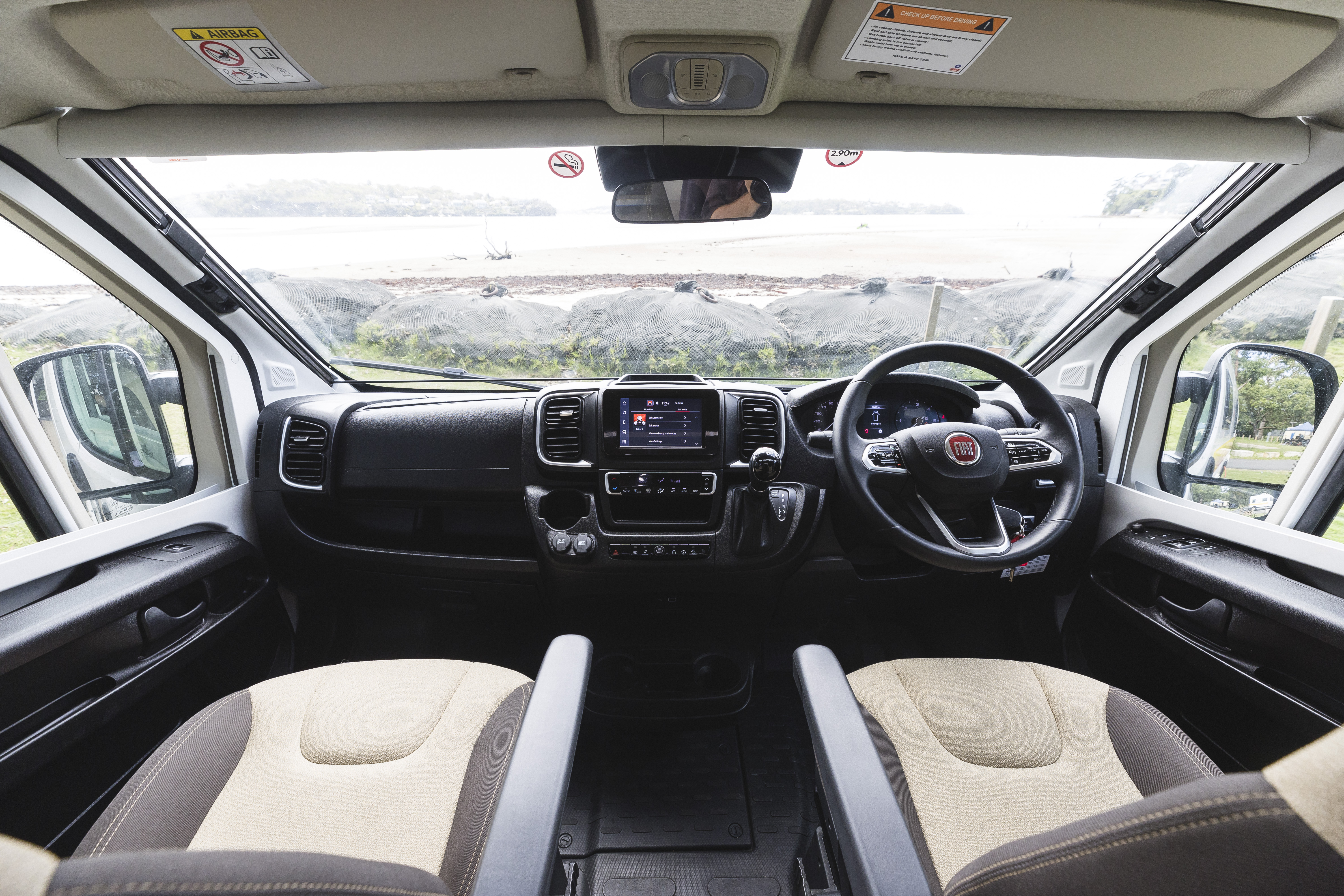 View of a modern campervan interior showing front seats, dashboard, steering wheel, and large front windows with scenic view.